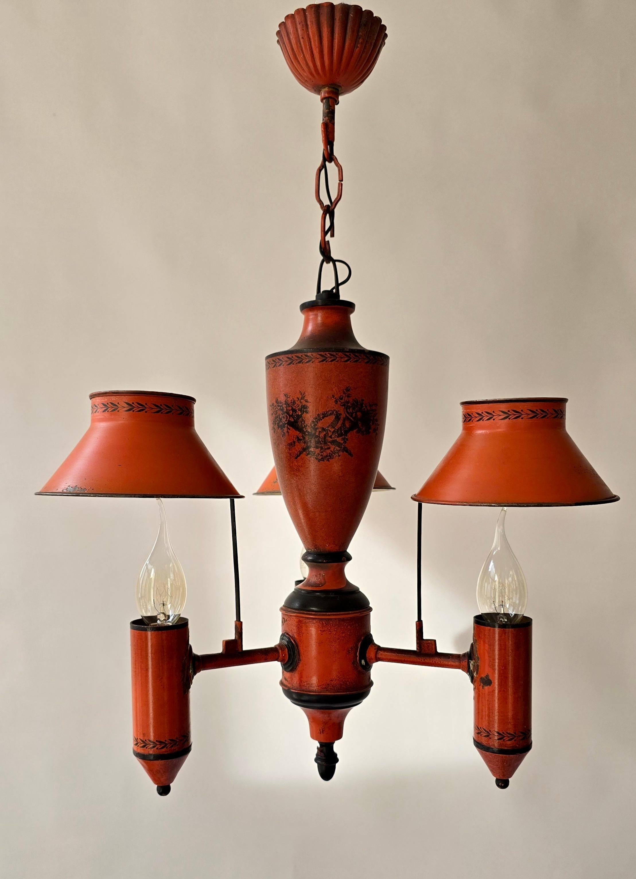 Red Neoclassical Tole Chandelier, Europe, ca. 1950

A striking vintage tole chandelier with three lights, featuring flared metal shades in warm red/orange with delicate black hand-painted decoration. The urn-shaped central body and Empire/Directoire