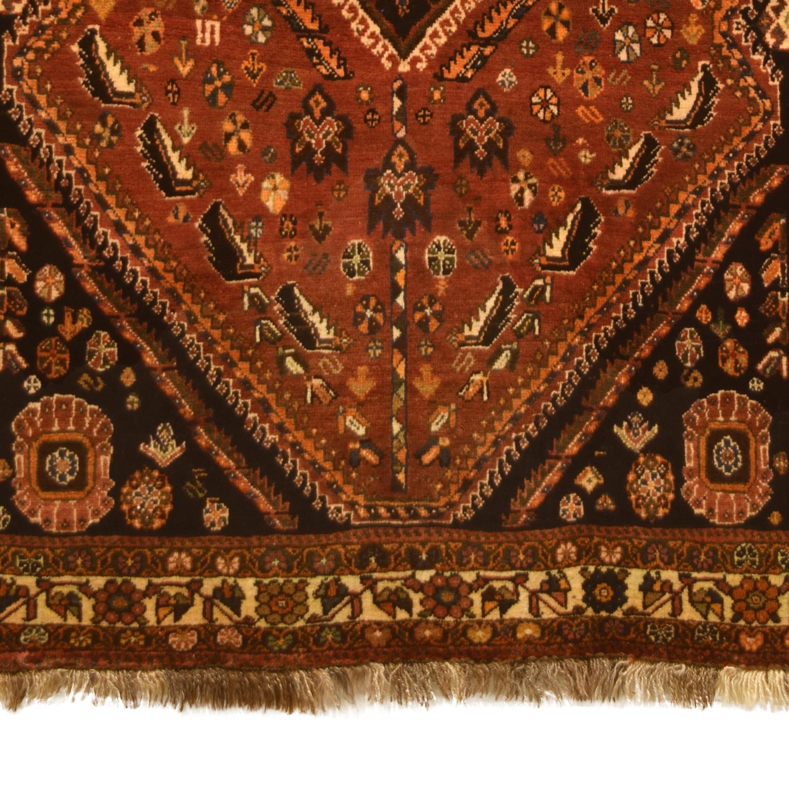 This semi-antique Persian Qashqai carpet is hand knotted in red, orange, brown, and cream wool. Crafted over 50 years ago, this classic Persian carpet remains in perfect condition. The traditional Persian weaving technique provides a plush pile and