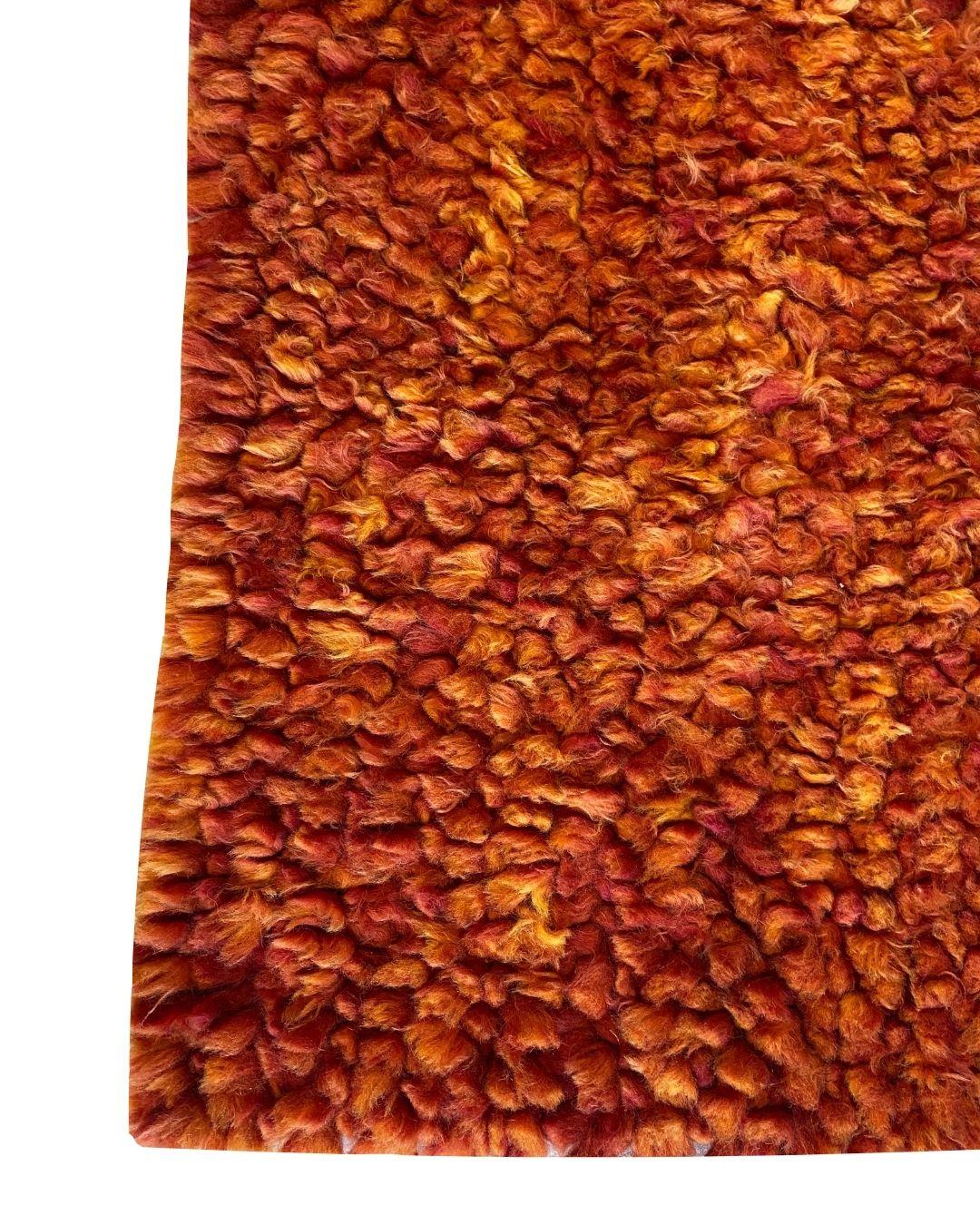 Esta alfombra anudada a mano en lana roja, naranja y amarilla, de 1,80 x 1,80 m, es una vibrante fusión de artesanía y sensibilidad de diseño moderno. Anudada a mano con lana 100%, esta alfombra de rica textura muestra una asombrosa mezcla de tonos