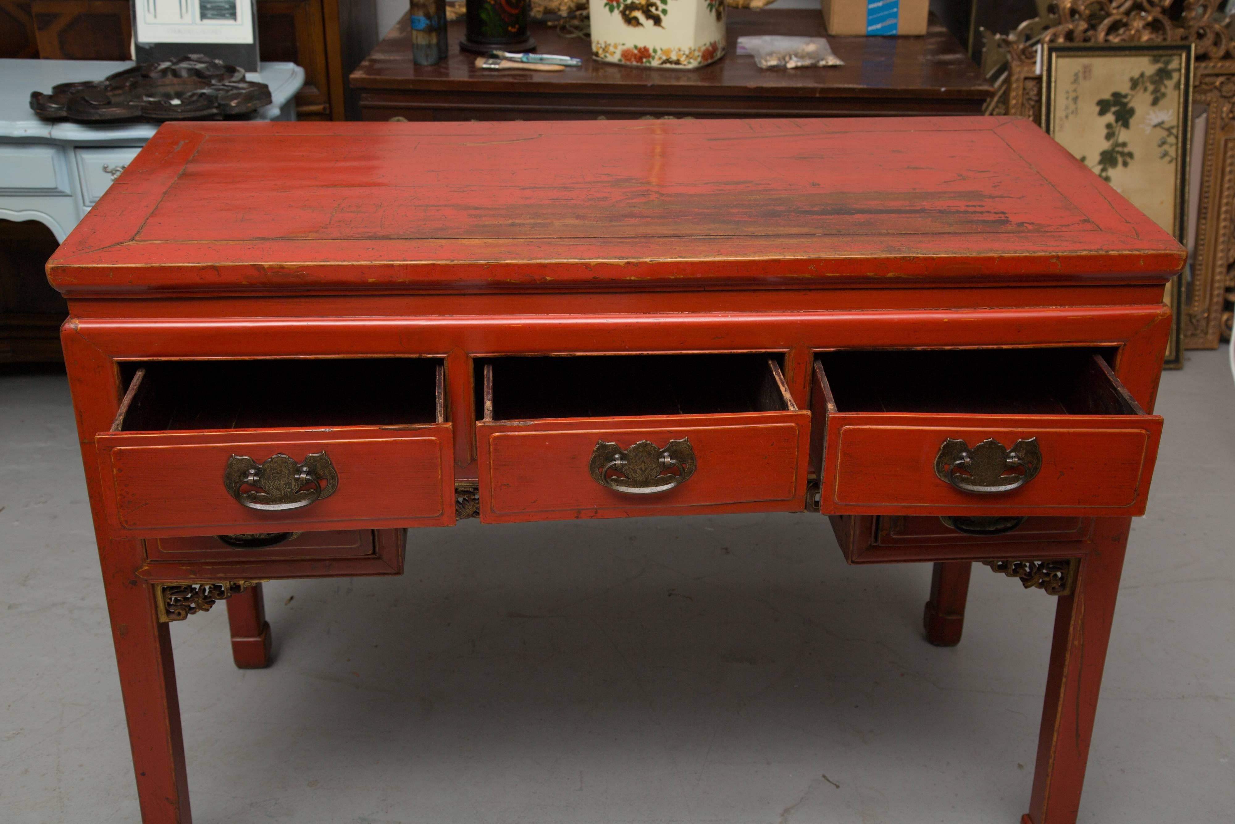 This is a very colorful red lacquered Chinese table. This case piece has a rectangular top over three frieze drawers above an opening flanked by two drawers, raised on straight block legs, 20th century.