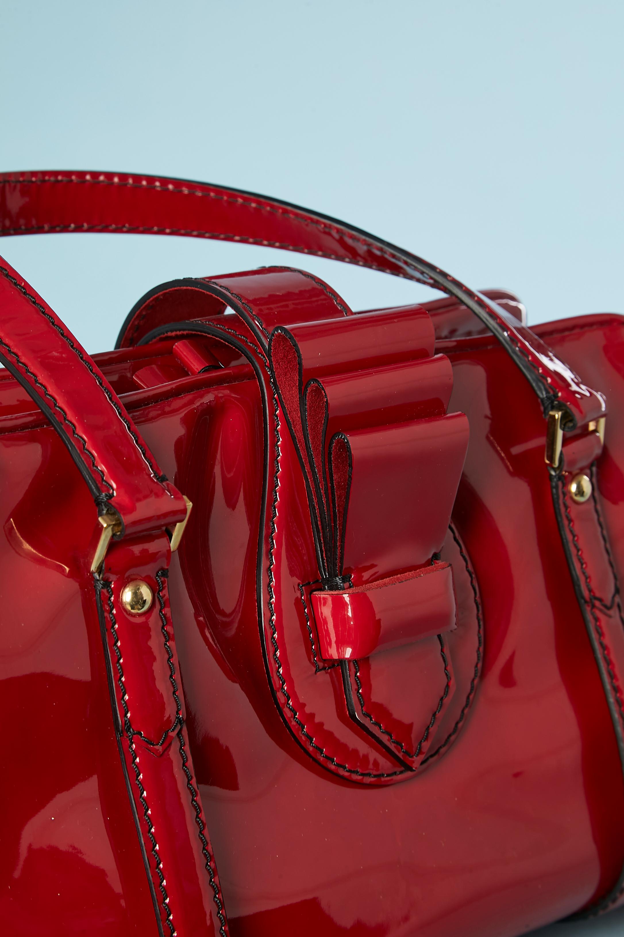 Red patent leather hand-bag . Red satin lining. Strap in red patent closure and zip underneath with 2 zip-puller. Black top-stitching. 2 compartiments inside separated by a pocket with zip. Inside this pocket there is 3 pockets ( 1 with zip and 2
