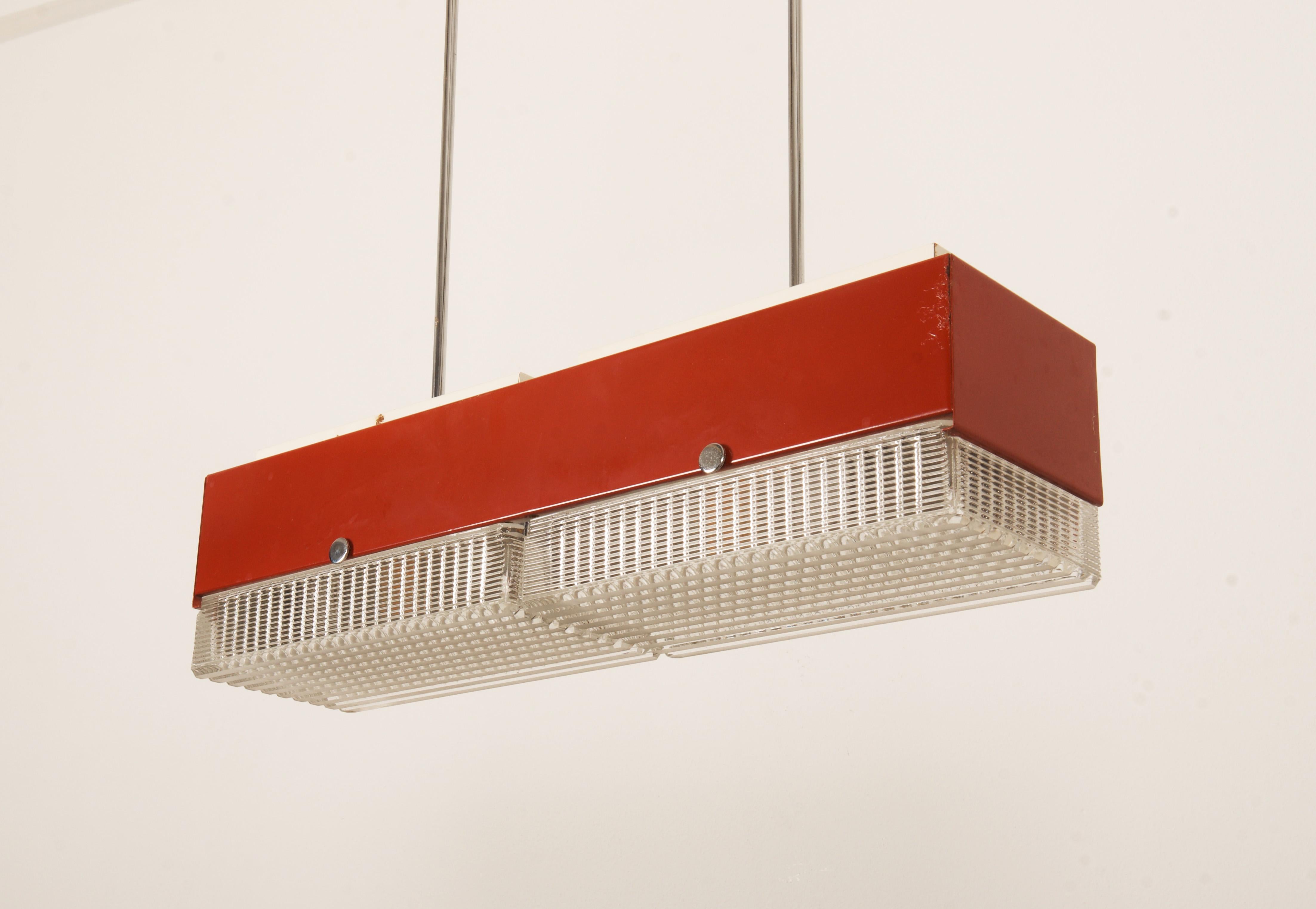 Struttura in acciaio verniciato rosso con due lampadine E27 da max. 100W ricoperte da un paralume in vetro pressato e raffinato dei primi anni Settanta.
La lampada può essere utilizzata come sospensione ma anche, dopo aver rifatto le aste, come