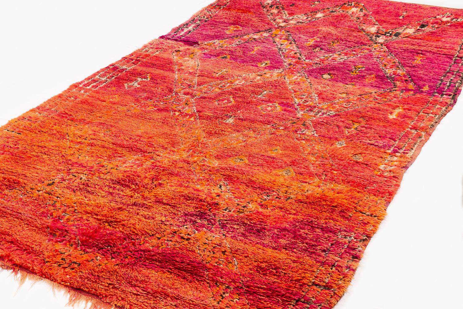 This antique vintage Moroccan rug came from the Beni Mguild tribe from the central middle Atlas mountains. This rug features beautiful dye, exhibiting rich color change in an ombre effect from glowing red and orange to a vibrant violet purple. It