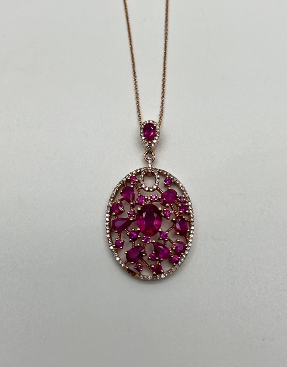 Questo splendido  ciondolo, presenta un intricato disegno traforato ornato da vibranti rubini rosa. La gemma ovale centrale è circondata da una disposizione armoniosa di pietre di varie forme, tutte incastonate in una delicata cornice in oro rosa.