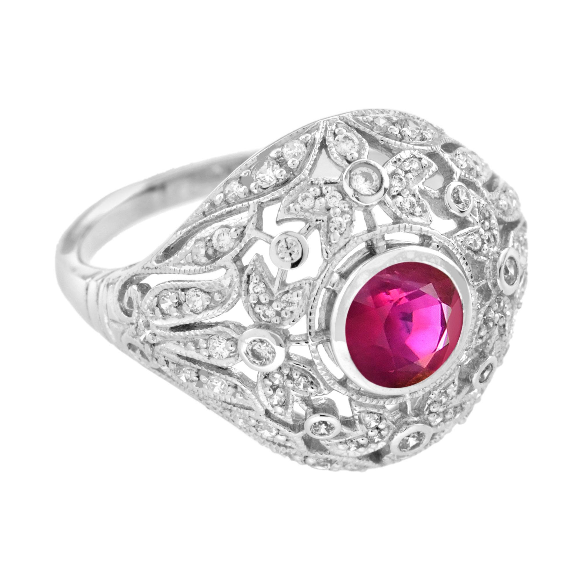 An Art Deco inspired engagement ring that features a bezel set round ruby. The center ruby is set in a dome mounting of open-work filigree, set with round diamonds. This ring is decorated with engraving with prominent leaf and floral motifs crafted