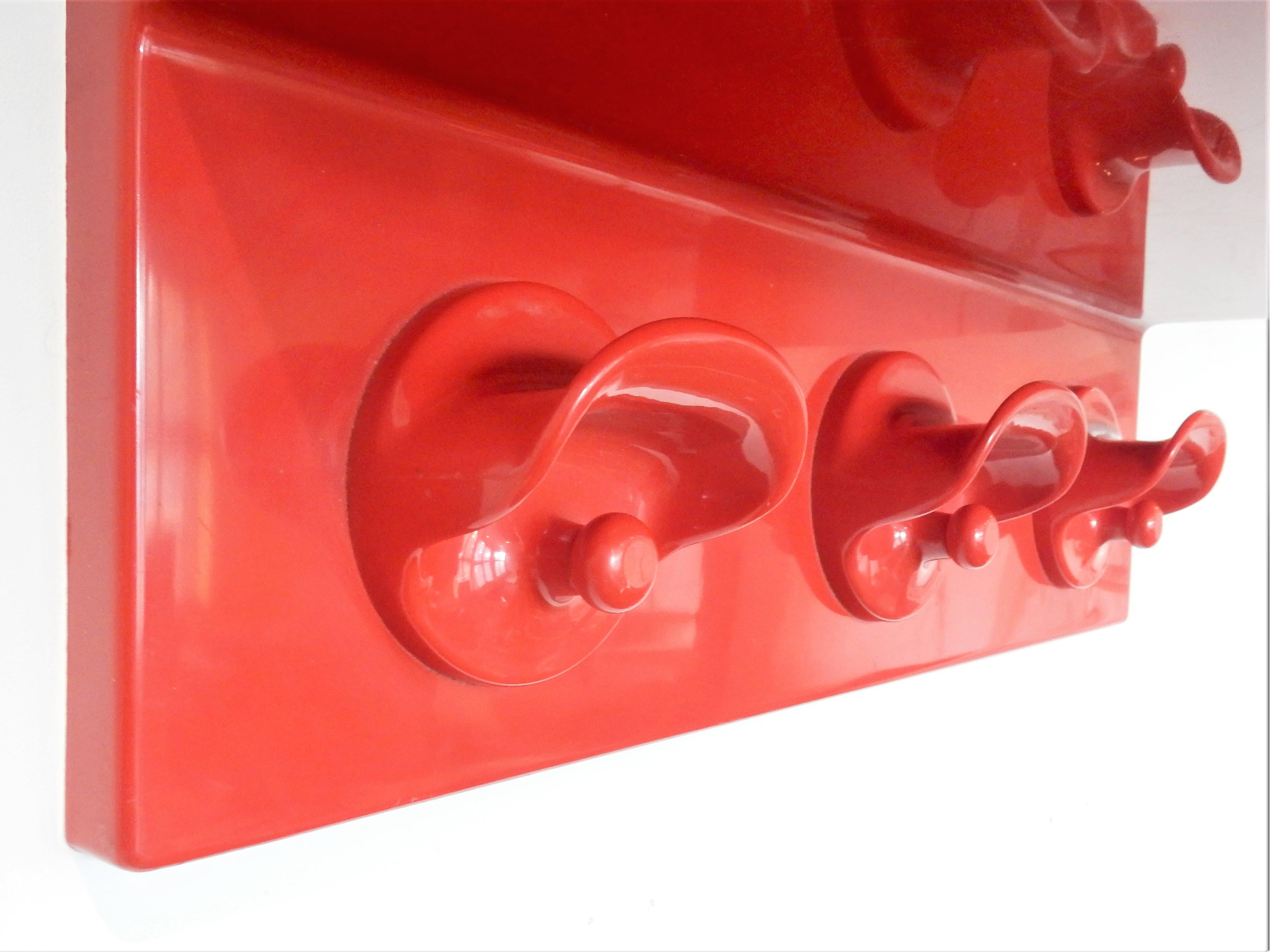 This moulded red ABS plastic coatrack with hooks and hat shelf was designed by Olaf von Bohr for Kartell in 1972. It has some light discoloration at the top of the shelf of lightly lighter circles. Very 1970s and a very nice eyecatcher in your