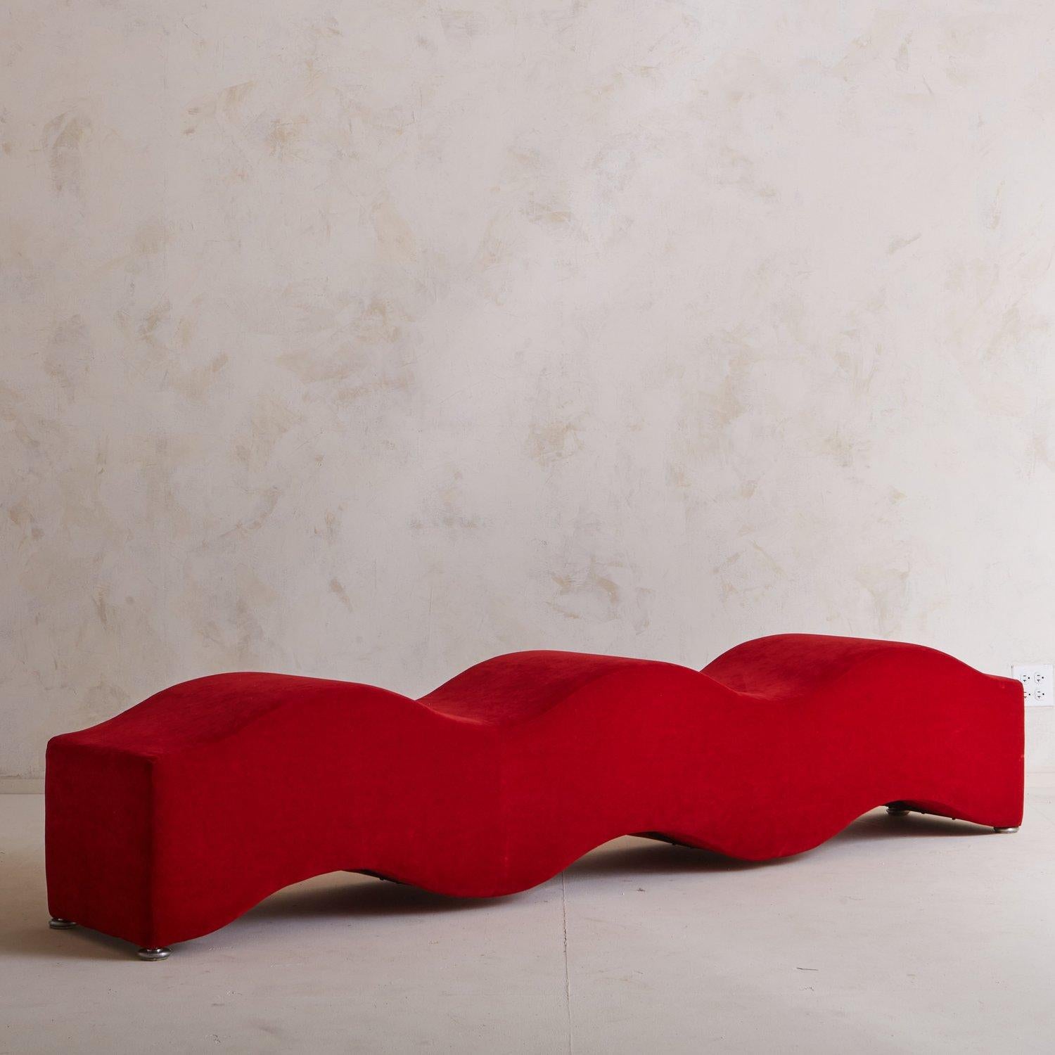 A playful curved bench featuring an organic form and vibrant red upholstery. This statement piece sits on four chrome feet that elevate it just slightly off the ground. Designed by Laurinda Spear for Coalesse. Spear (1950—) is an American architect