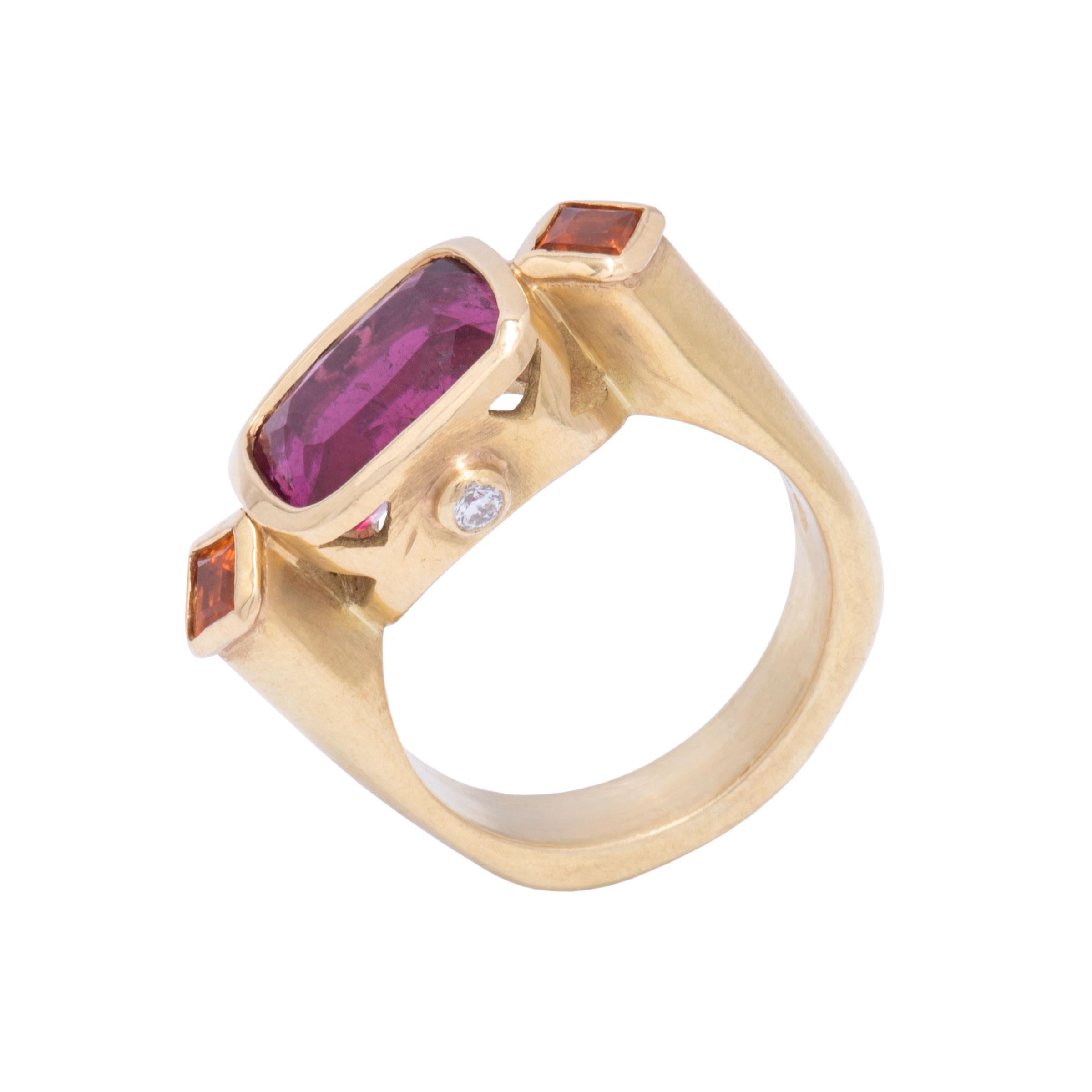 A ruby red Rubellite Tourmaline 3.99 cts  is centered between two bright orange square cut spessartine garnets. The cut profile of this ring in satiny 18 karat gold is set on either side with .06cts round white diamonds. A molded band squares gently