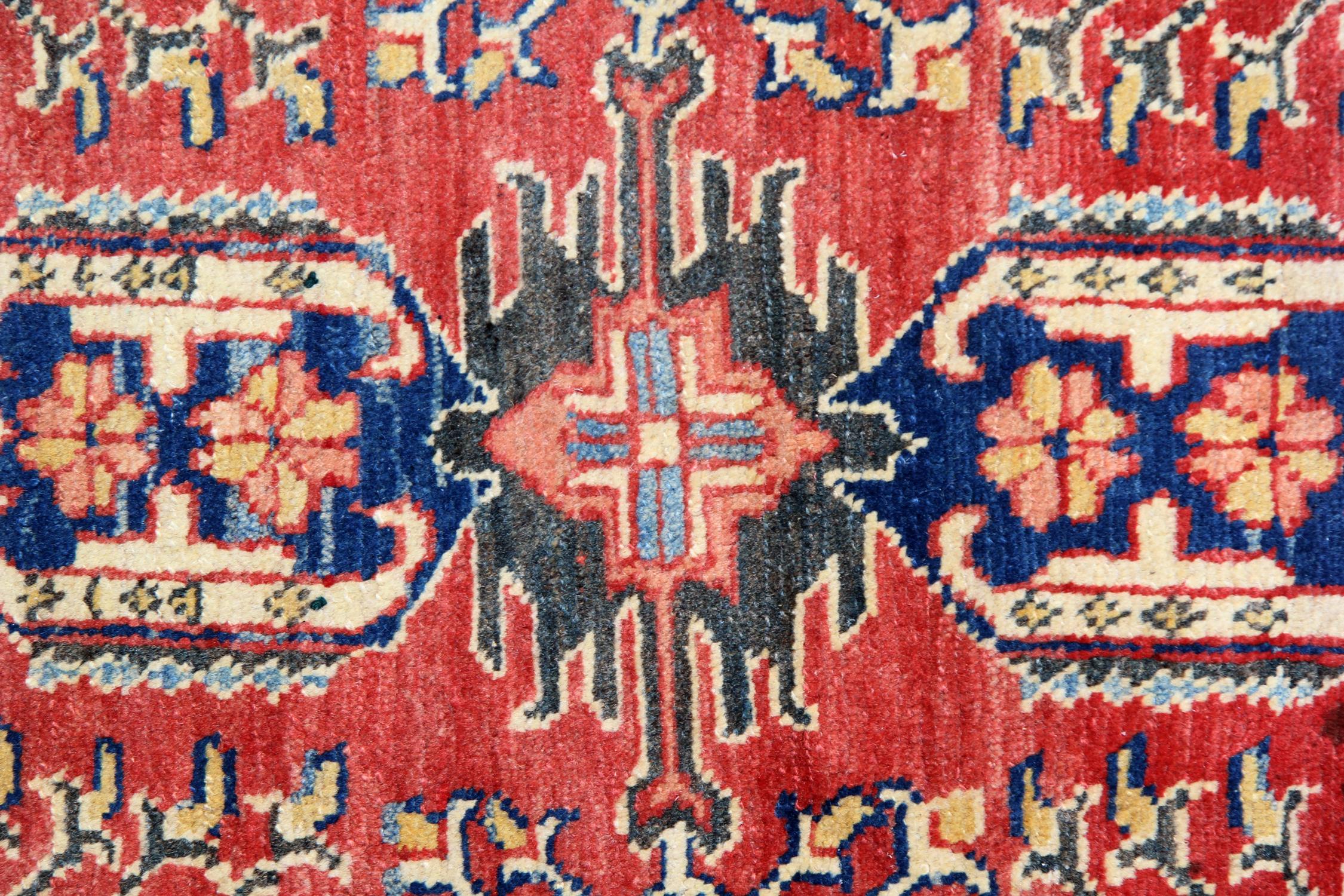 This fine wool rug was woven by hand in Afghanistan in the 1995s. The central design features a traditional geometric motif design woven in accents of cream blue and green on a rich red background. Both the colour and style in this piece are sure to