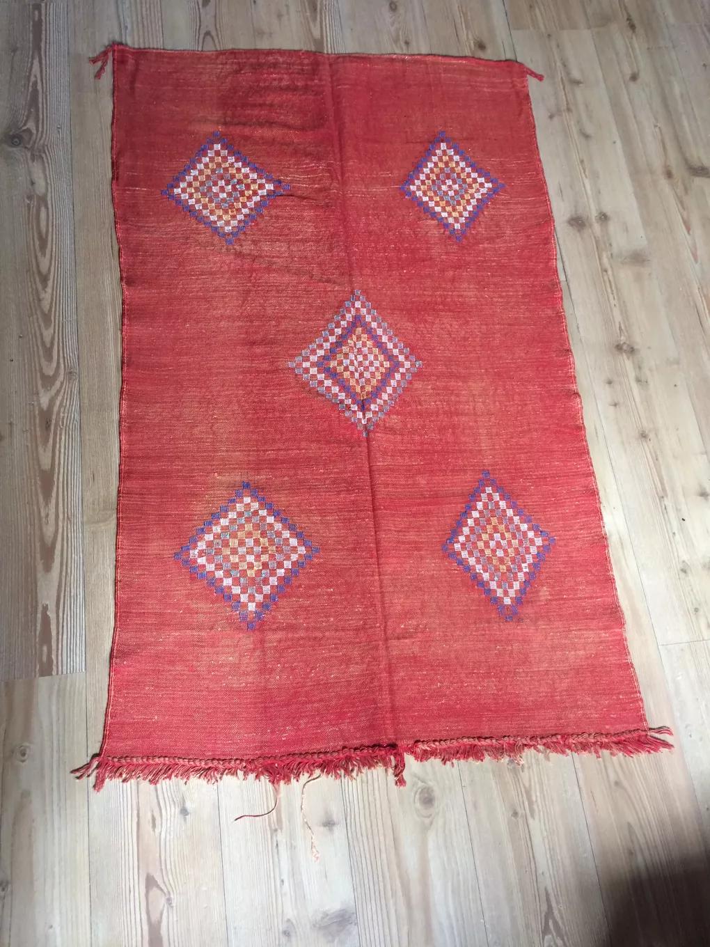 Ce tapis Kilim marocain sabra de fabrication exquise présente des motifs berbères noués sur une base tissée en une seule couleur. Fabriqué entièrement en soie végétale. Tapis tissé et noué à la main. Mesures : 85 x 145 cm.