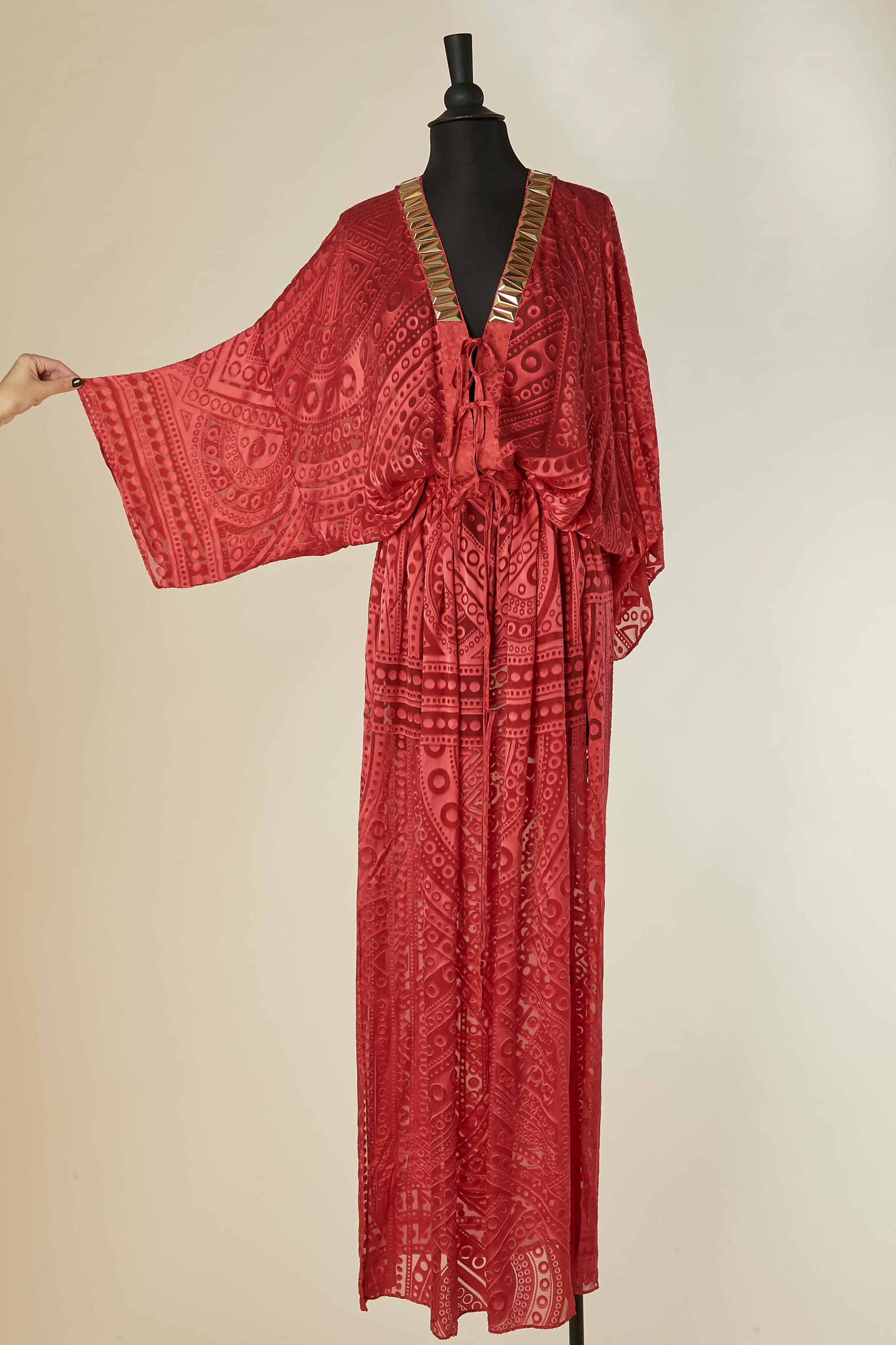 Rotes, durchsichtiges Abendkleid mit goldener Plastikverzierung am Dekolleté.
Zusammensetzung des Stoffes: 63% Viskose, 37% Seide. Kordelzug in der Taille und Schleifenverschluss in der vorderen Mitte. Schlitz und Tasche auf beiden Seiten.