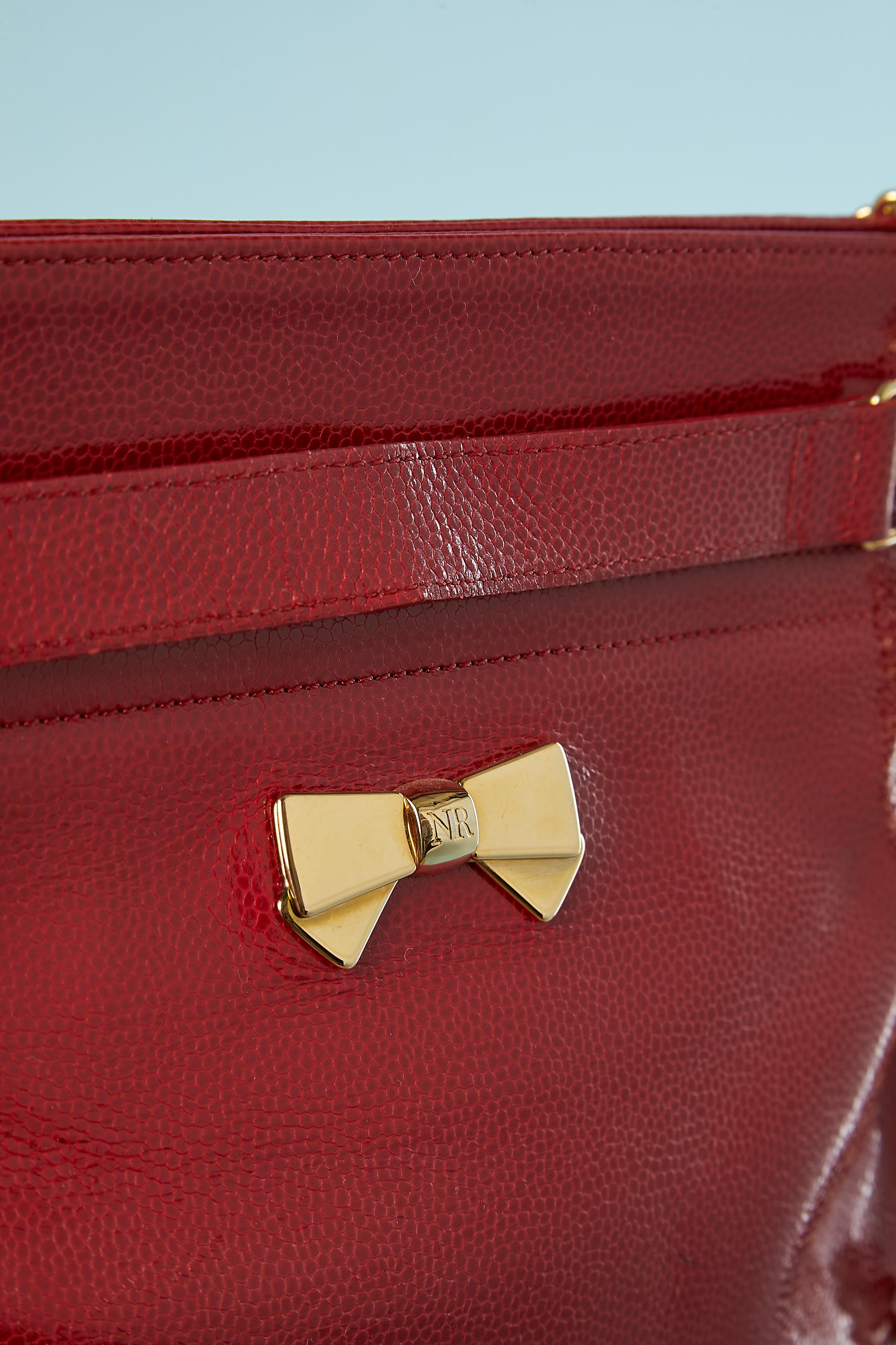 Rote Umhängetasche aus glänzendem Leder mit goldener Metallkette und Schleife. 
Schnappverschluss. 1 Tasche mit Reißverschluss innen. Schwarzes Lederfutter. Staubbeutel wird mitgeliefert.
Größe: 28 cm X 26 cm X 10 cm