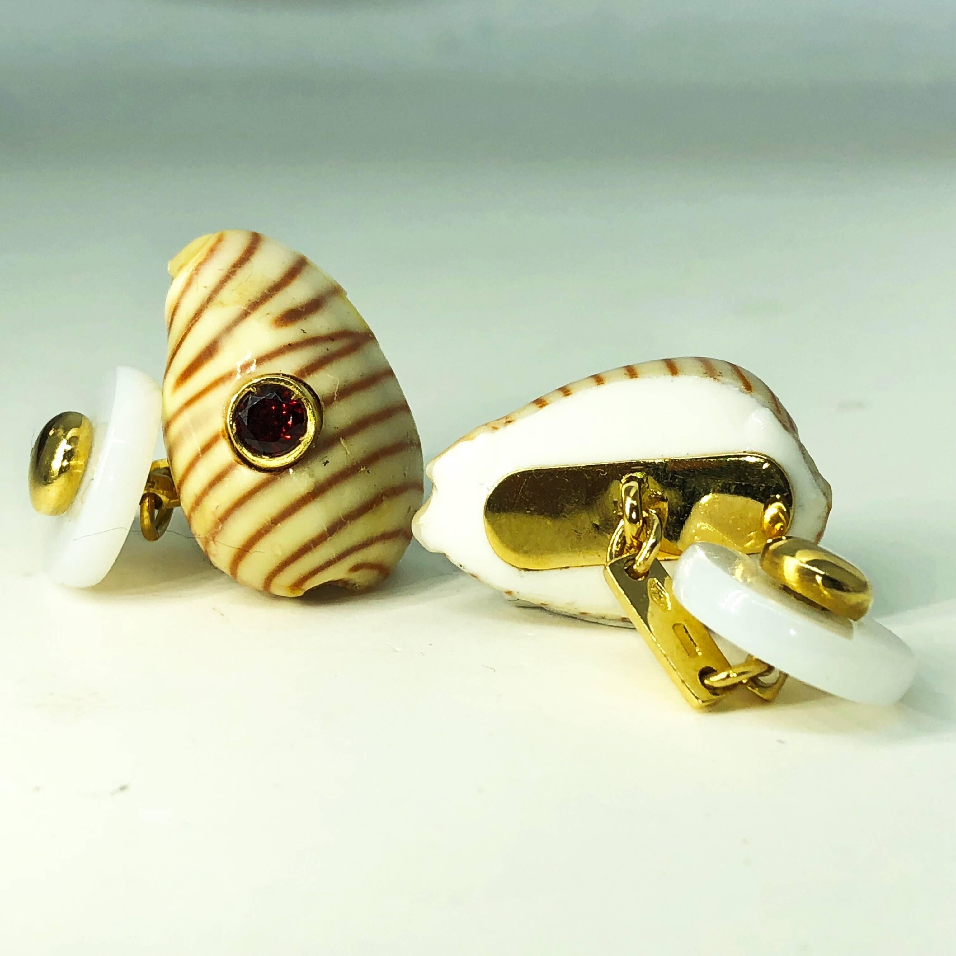 Unique pair of cufflinks combining a beige and carnelian red stripes seashell shaped with the magic vivid red of spessartine and a chic hand inlaid white agate disk back, 18Kt yellow gold setting.
In our smart tobacco suede leather box and Pouch.