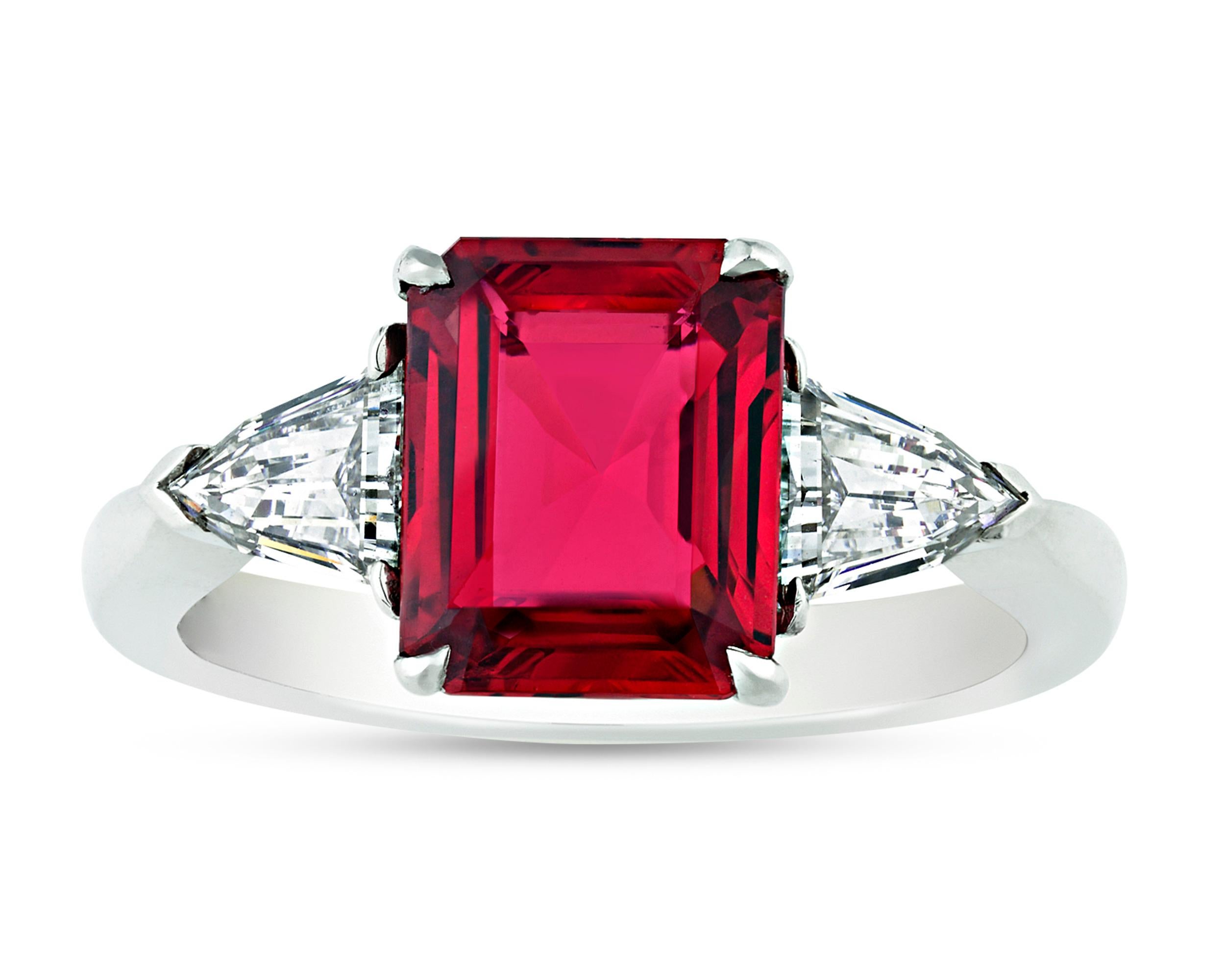 A crimson red, emerald-cut spinel weighing 2.03 carats is joined by a pair of white, triangular diamonds totaling 0.60 carat. The vibrant central gem is certified by the Gemological Institute of America as a natural Burmese spinel. Set in platinum.