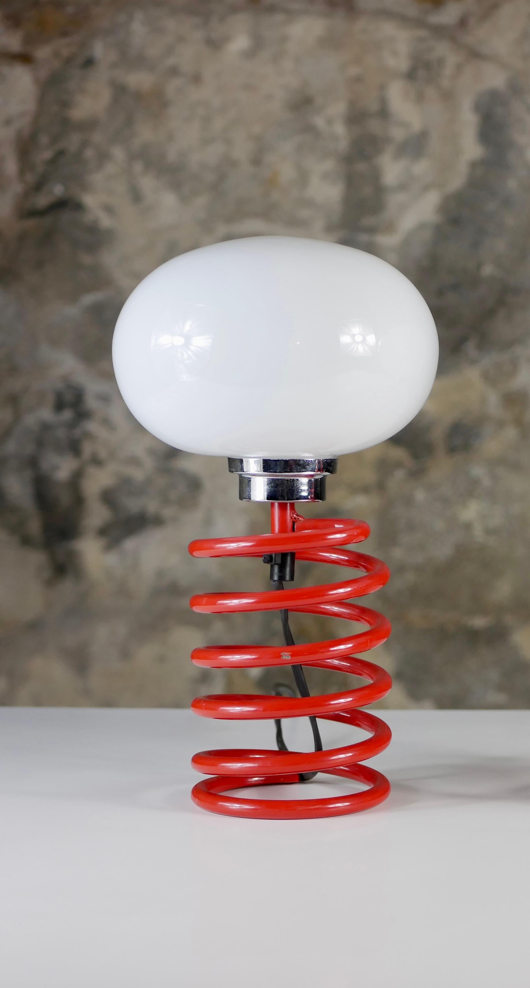 Beautiful and rare spring table lamp attributed to Ingo Maurer, made in Germany in the 1970s.
Red lacquered metal spiral with original opaline glass.
Very good condition, light scratches on spring.
Dimensions : H31cm, D17cm

2 available.