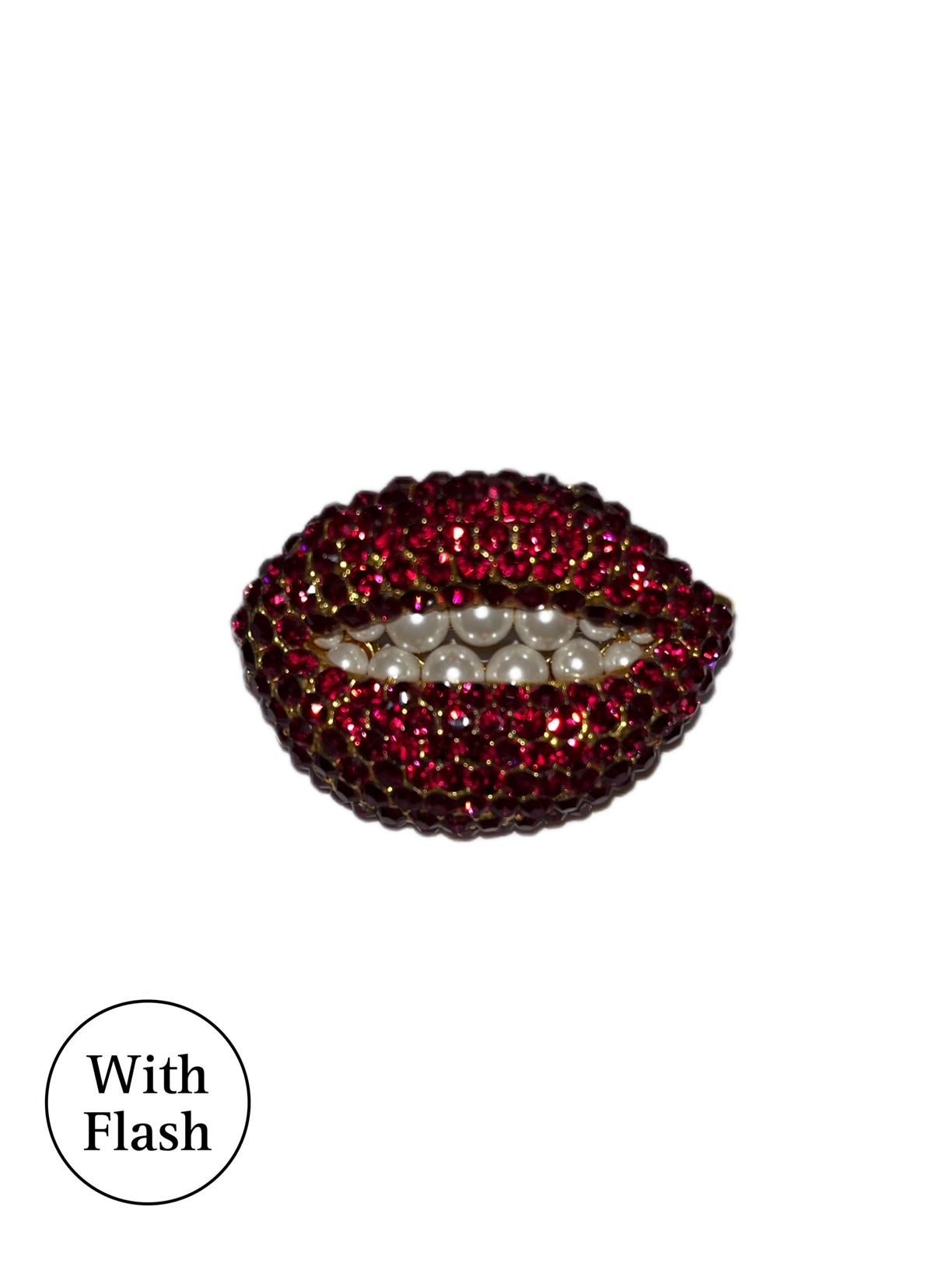 This surrealist lip brooch is inspired by the famous Spanish painter Salvador Dalí­. The brooch is shaped like a lip, with red rhinestones imitating lipstick and faux pearls as the teeth. The brooch is made of brass with a gold plate. Inside the
