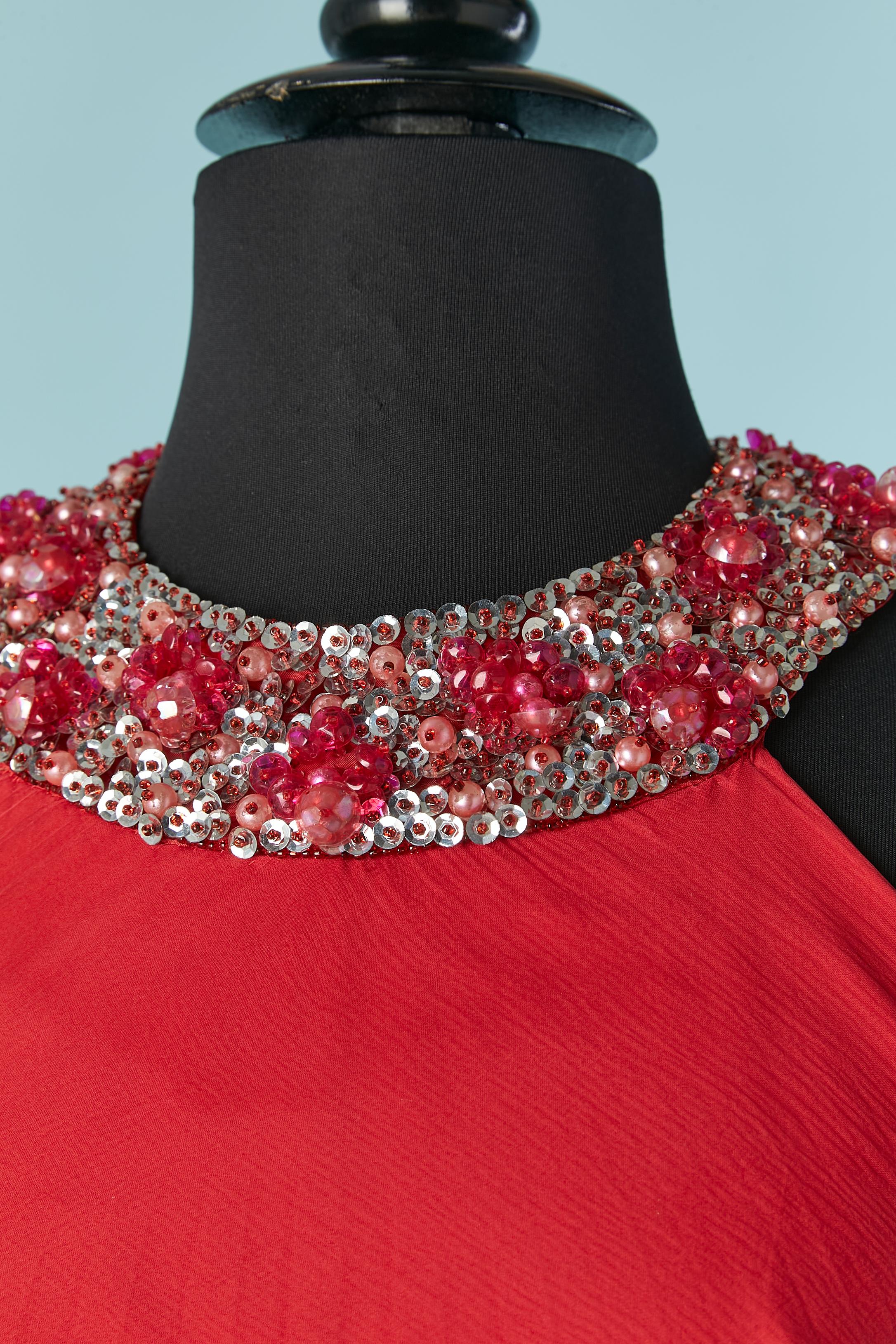 Vestido de noche rojo plisado con lentejuelas y pedrería. No hay etiqueta de composición del tejido en el interior del vestido, pero probablemente sea gasa de seda y forro de rayón.
Cierre a presión y cremallera en la parte central de la espalda.