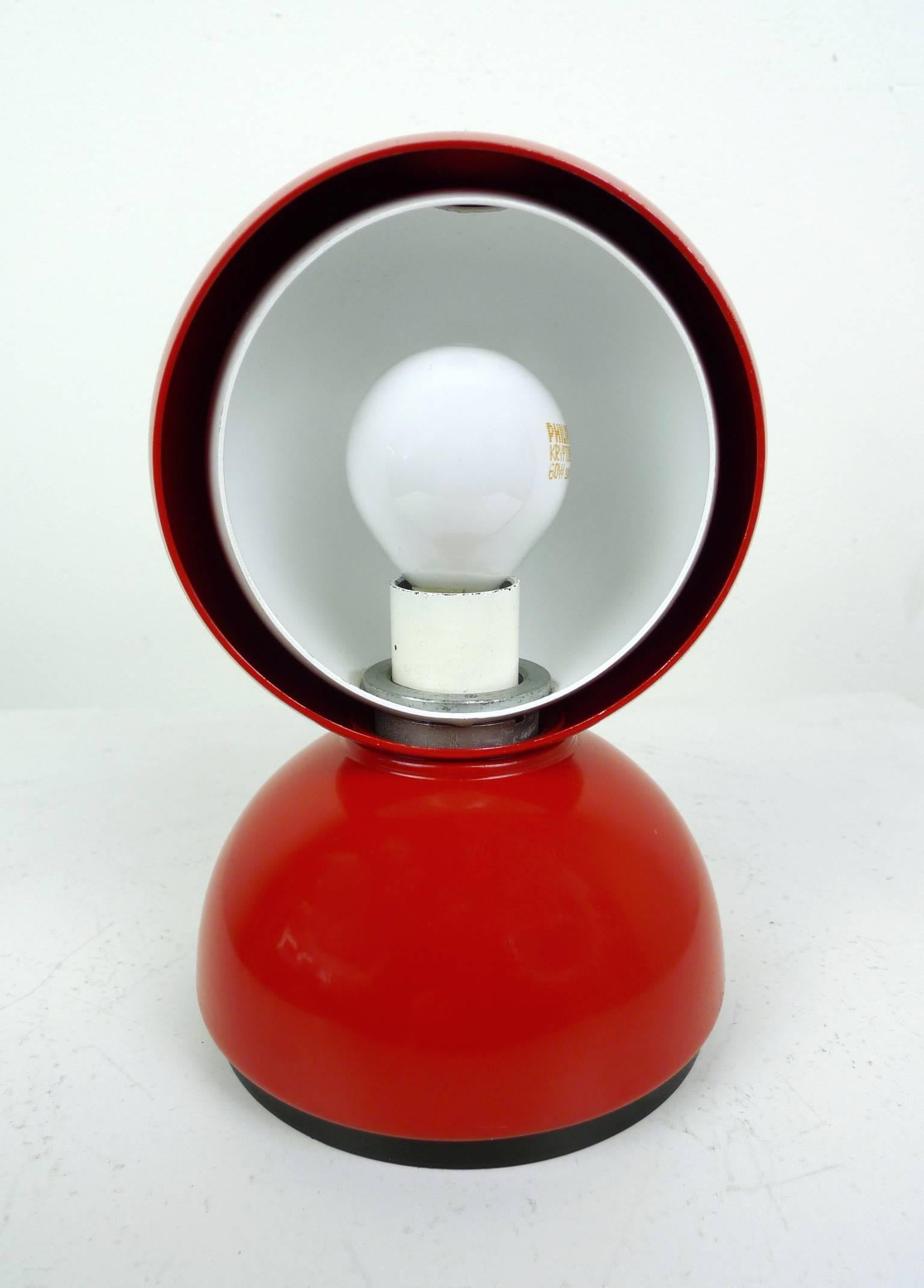 This Eclisse table or wall lamp was designed in 1967 by Vico Magistretti and produced by Artemide in Italy. The red-painted metal body surrounds a white hemisphere, which regulates the light intensity. The effect of the light is modeled on the moon