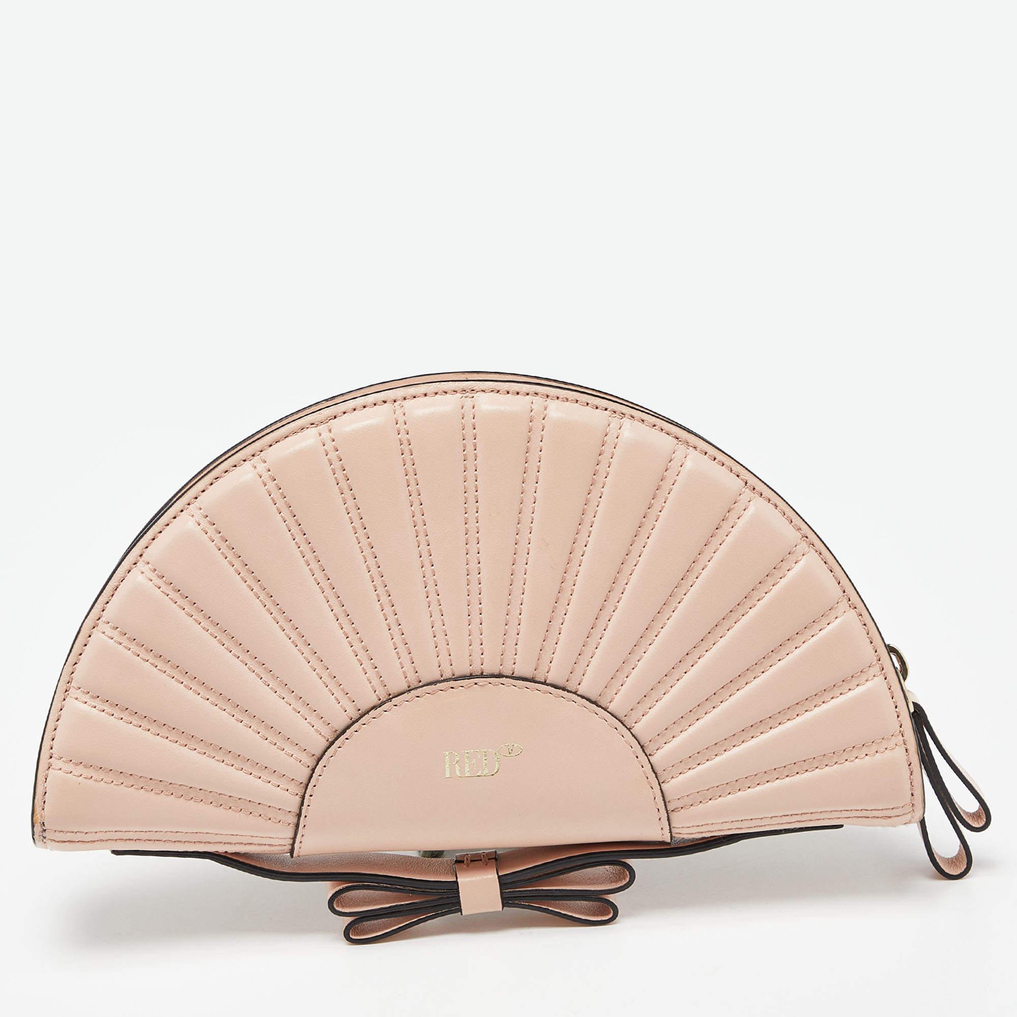 The RED Valentino clutch is an exquisite accessory, crafted from supple peach-hued leather. Its elegant shell shape is adorned with a prominent bow, adding a touch of femininity. The compact design makes it a versatile and stylish companion for any
