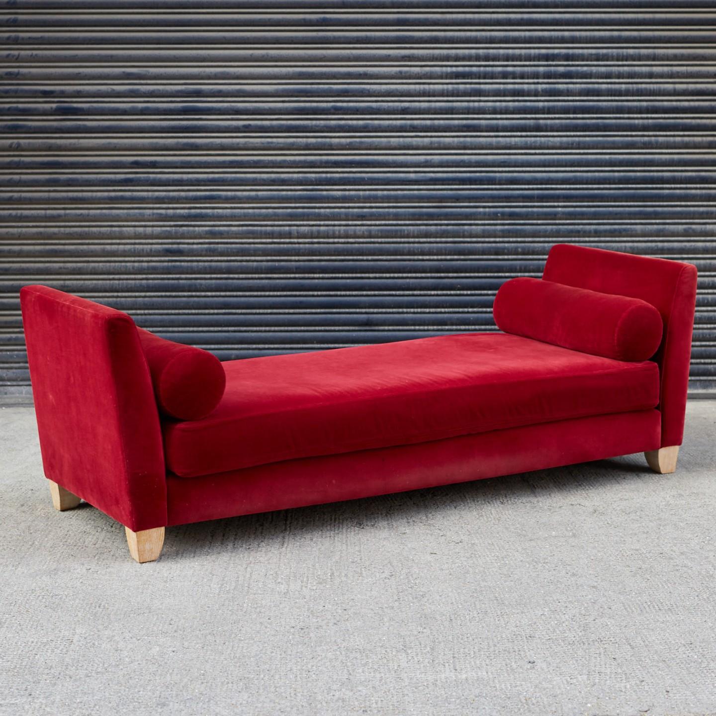 A red velvet upholstered daybed sofa with limed oak feet.