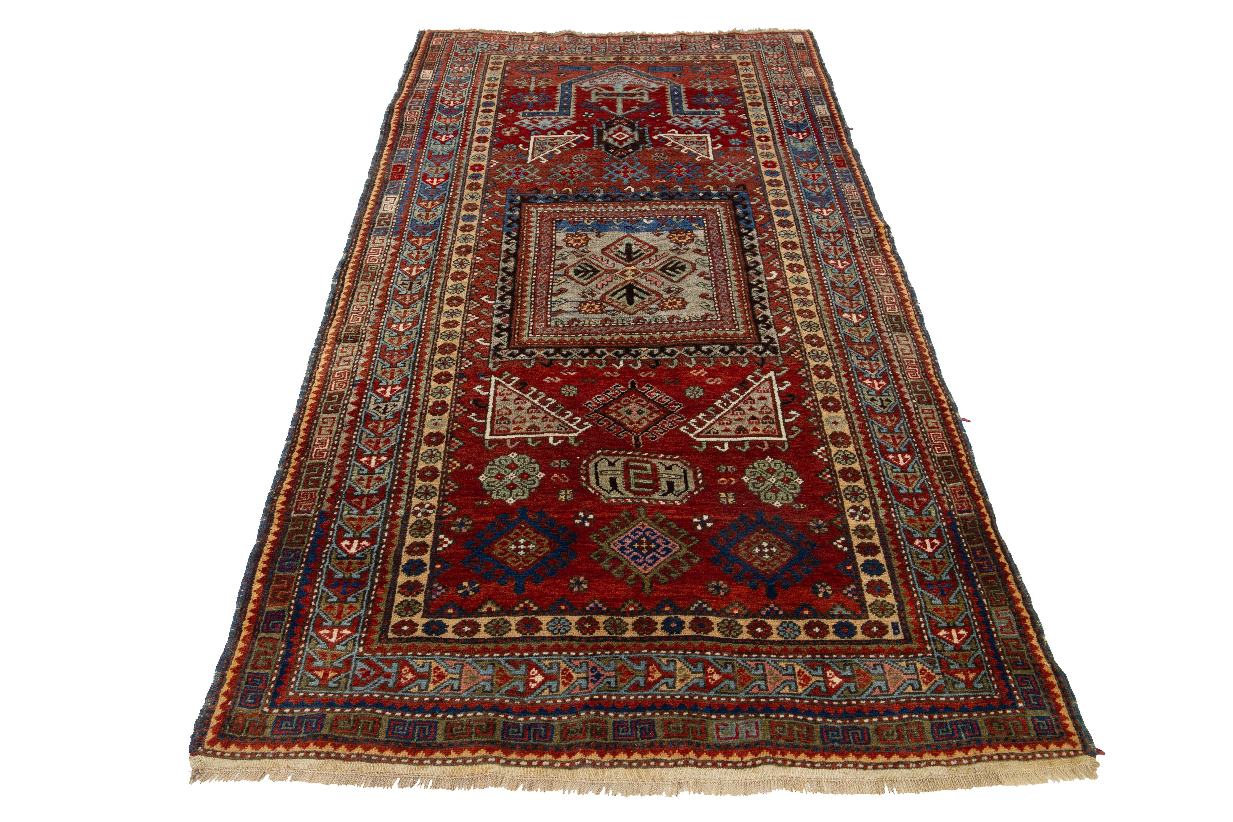 This handcrafted Kazak wool rug features a vibrant red palette with delicate green, blue, and beige accents. The center of the piece is adorned with an intricate geometric pattern.

This rug measures 4'1'' x 7'3''.