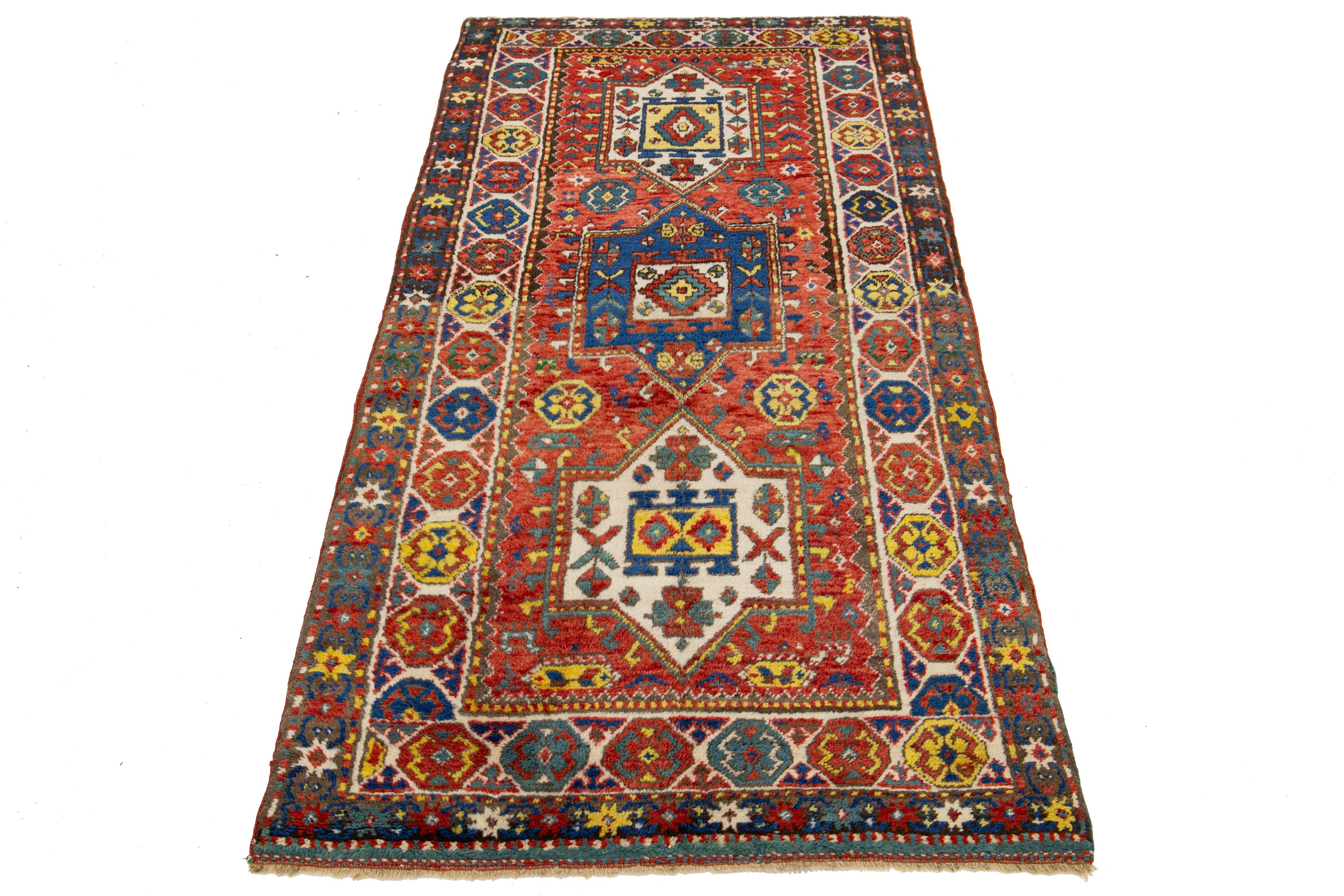 Dieser handgefertigte Teppich aus kasachischer Wolle zeigt eine lebhafte rote Farbpalette mit zarten blauen, gelben und beigen Akzenten. Es ist mit einem komplizierten Allover-Muster verziert.

Dieser Teppich misst 3'4'' x 6'10''.