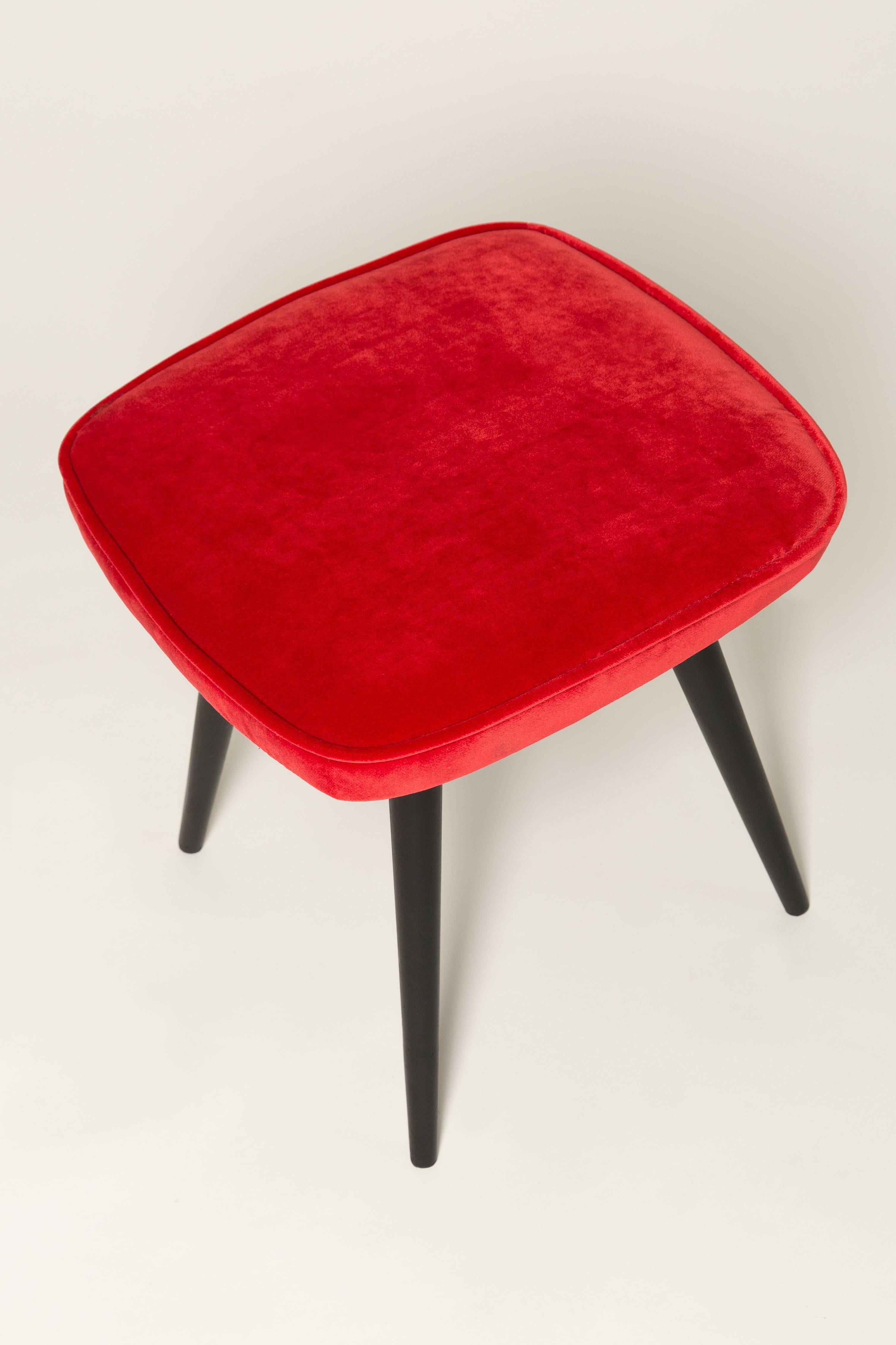 Hocker aus der Zeit um die 1960er und 1970er Jahre. Schöne rote Samtpolsterung. Der Hocker besteht aus einem gepolsterten Teil, einer Sitzfläche und sich nach unten verjüngenden Holzbeinen, die für den Stil der 1960er Jahre charakteristisch sind.
