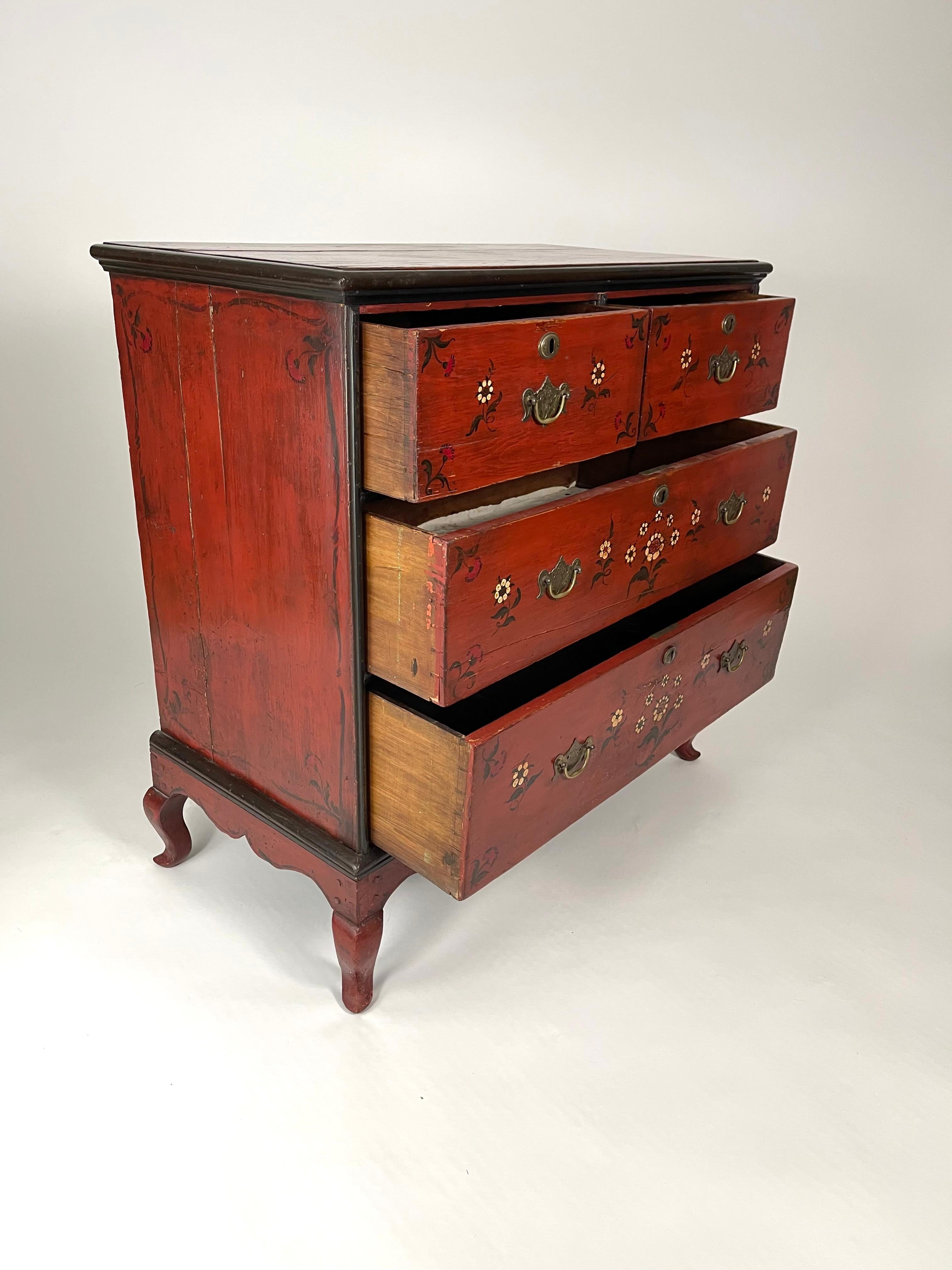 A charming red floral painted Queen Anne style chest of drawers, with painted black trim and stylized black cream and red flowers, with three long drawers each with engraved brass drawer pulls, the lock bearing the WR cypher of King William IV, with