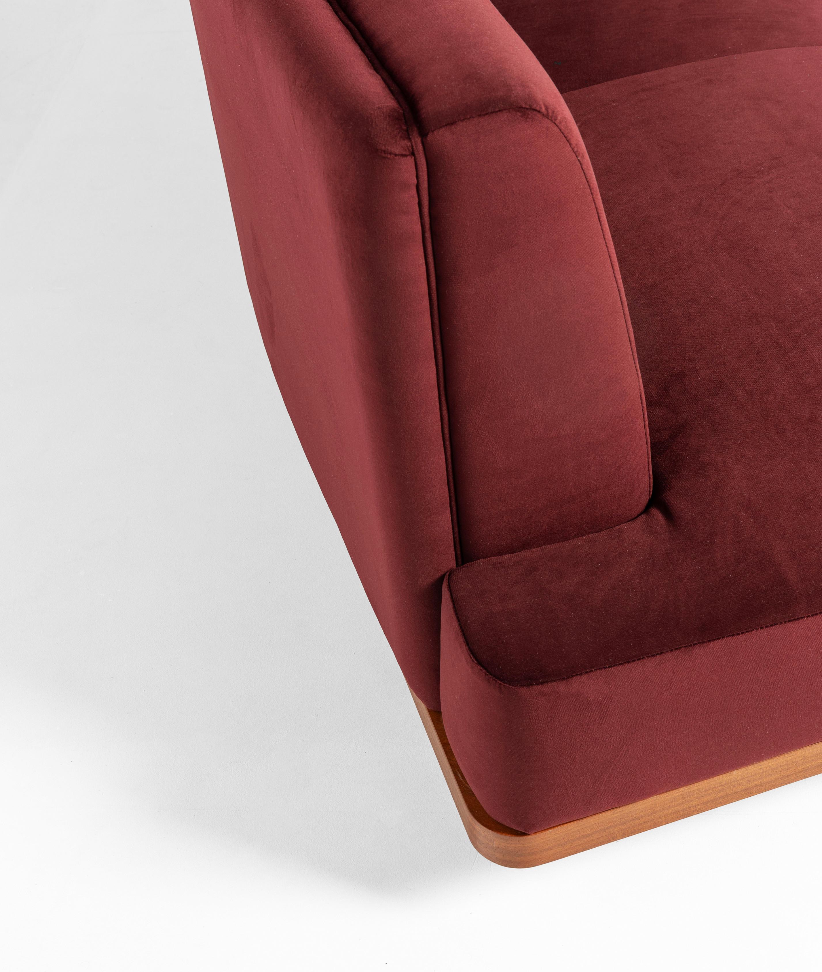 This medium-sized sofa by Lorenza Bozzoli features a distinctive curved silhouette upholstered in rich red wine velvet, combining modern style with comfort. Attached to its rear is a mahogany cabinet with two doors, detailed with an elegant