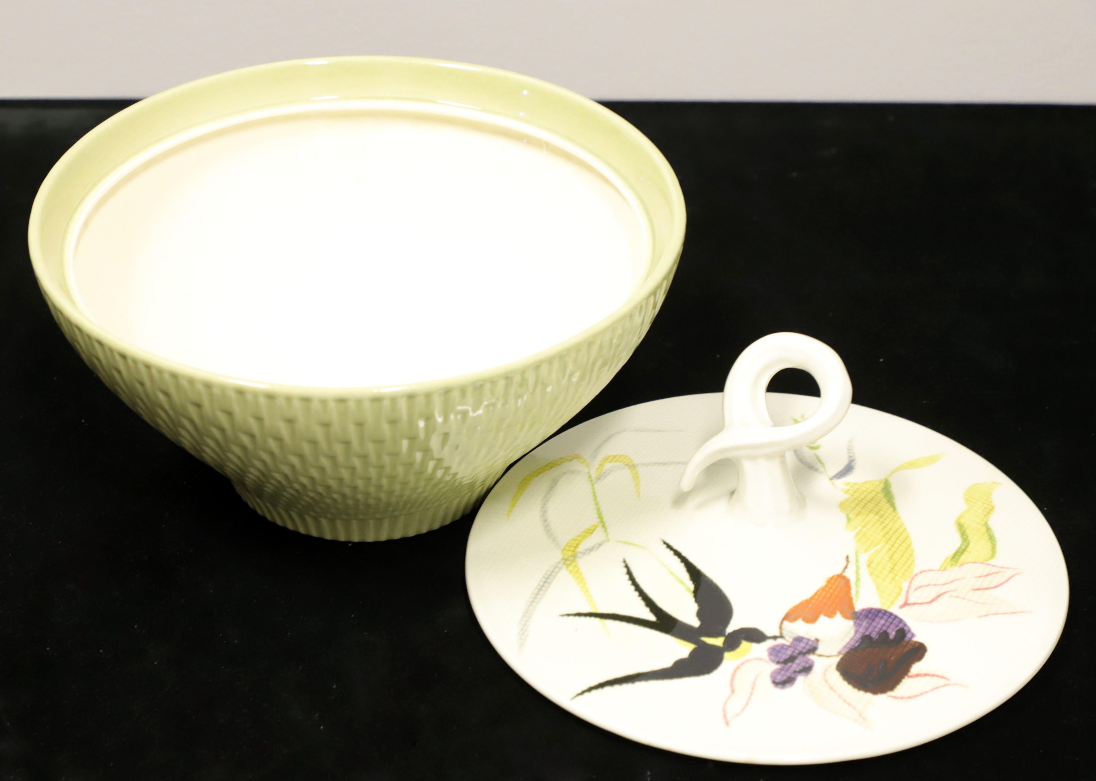 A Mid 20th Century serving bowl with lid by Red Wing, in their Capistrano pattern. Bowl has a round shape, smooth cream color interior and sage green color basket weave exterior. Lid has a unique curled stem-like handle and is hand painted depicting