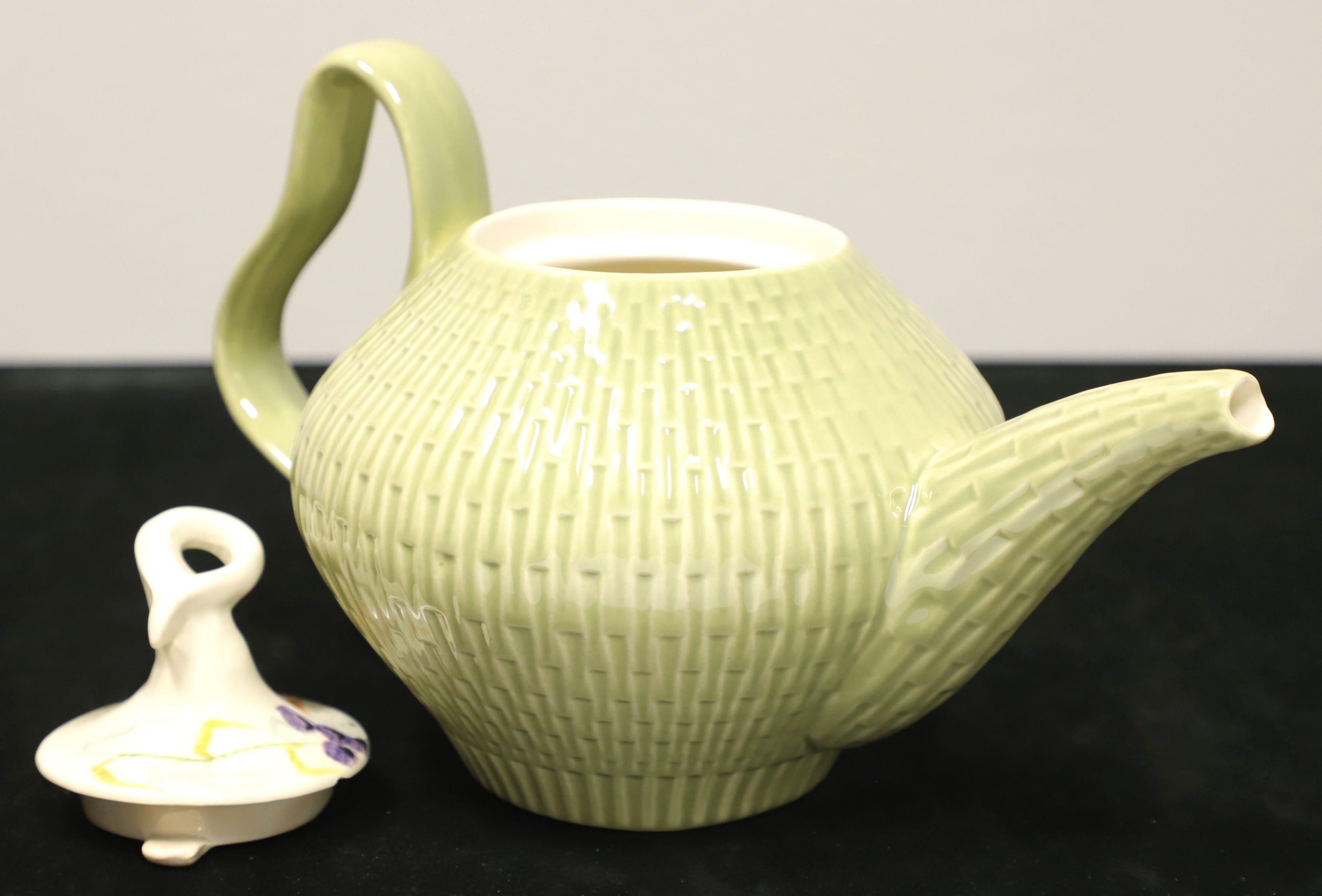 A Mid 20th Century tea pot with lid by Red Wing, in their Capistrano pattern. Pot has a round shape, smooth cream color interior and sage green color basket weave exterior, pour spout & handle. Lid has a unique curled stem-like handle and is hand