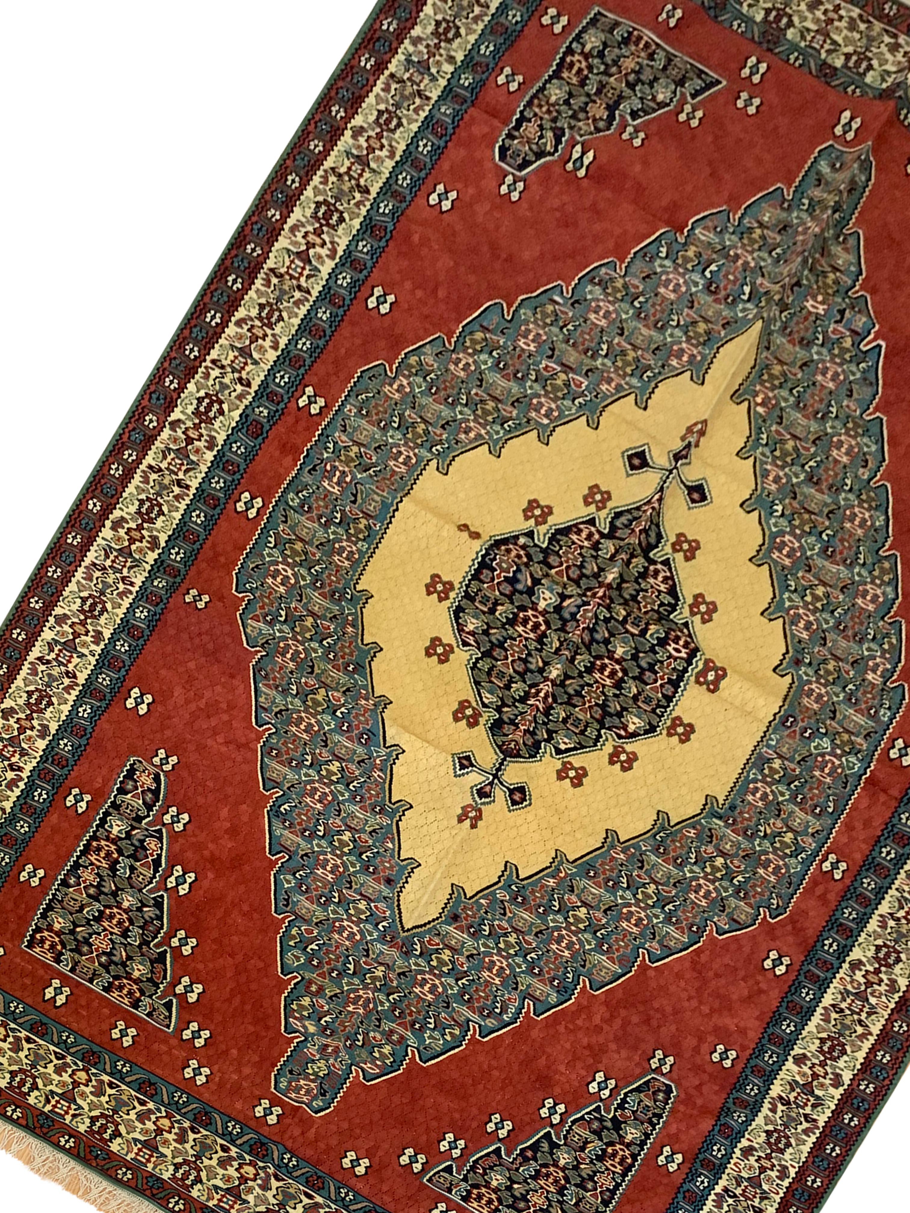 This beautiful flatwoven area rug is a Kurdish kilim woven in the early 2000s, circa 2010. Constructed with only the finest organic materials. The design features a bold red background with a large decorative medallion woven in accents of green and
