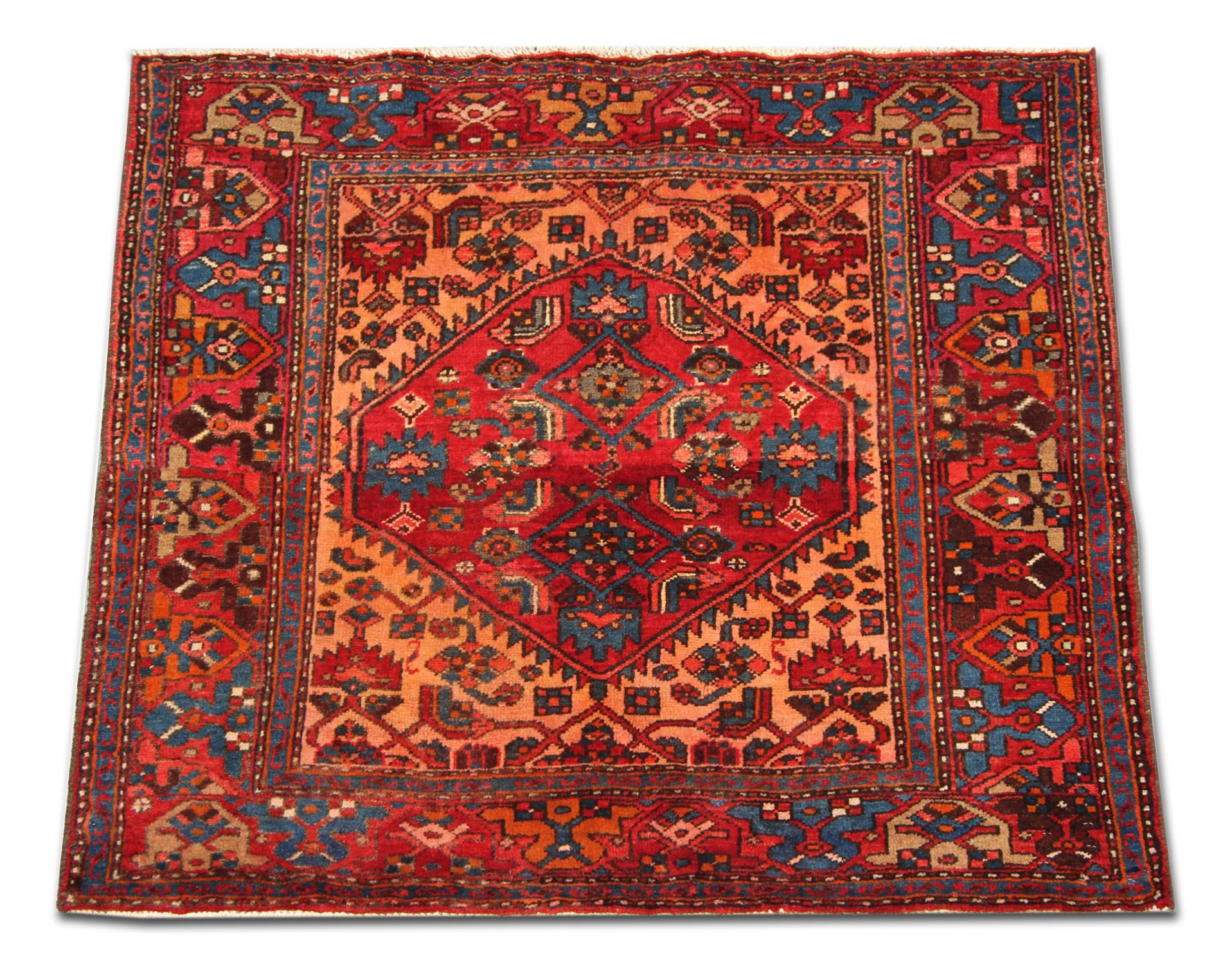 Dieser Teppich aus feiner Wolle wurde mit edlen Materialien von Hand gewebt und zeigt eine reiche Farbpalette aus Rot, Orange, Beige und Blau, die zu einem symmetrischen Stammesmuster gewebt wurden. Das zentrale Medaillon und das umgebende Design