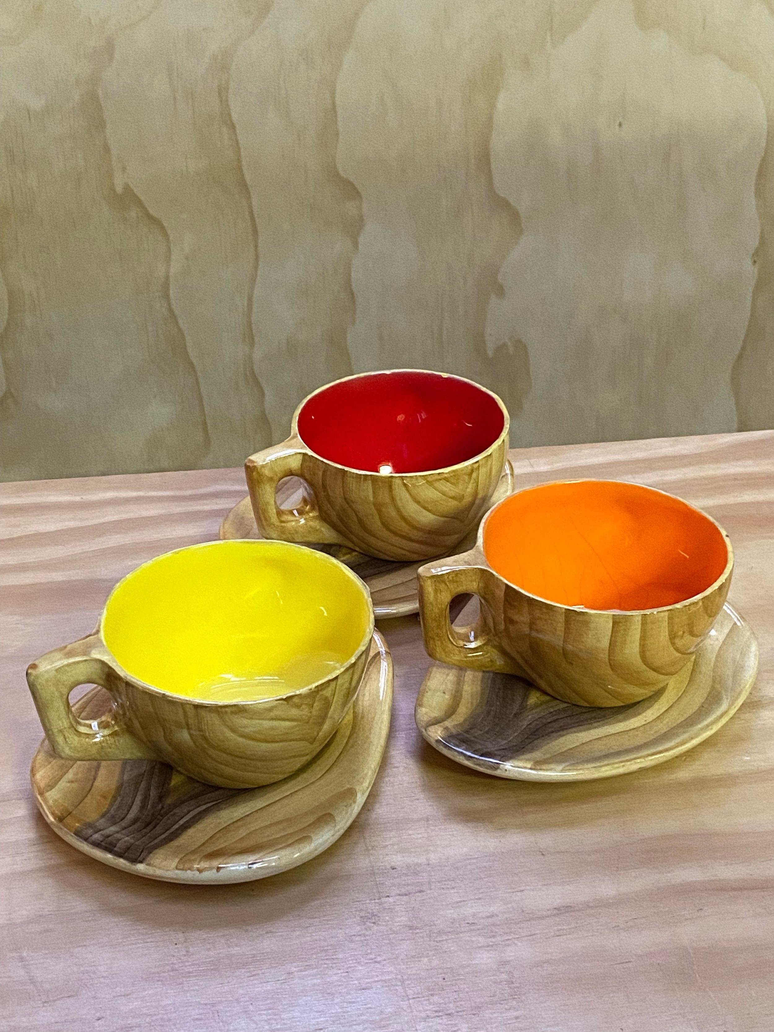 Trio of fun coffee or hot chocolate cups and saucers, painted to resemble wood, with strong Red, Yellow and Orange glazed interiors. 

Designed by French ceramicist, Eugène Grandjean. These don’t have the Vallauris mark, but they’re a good period