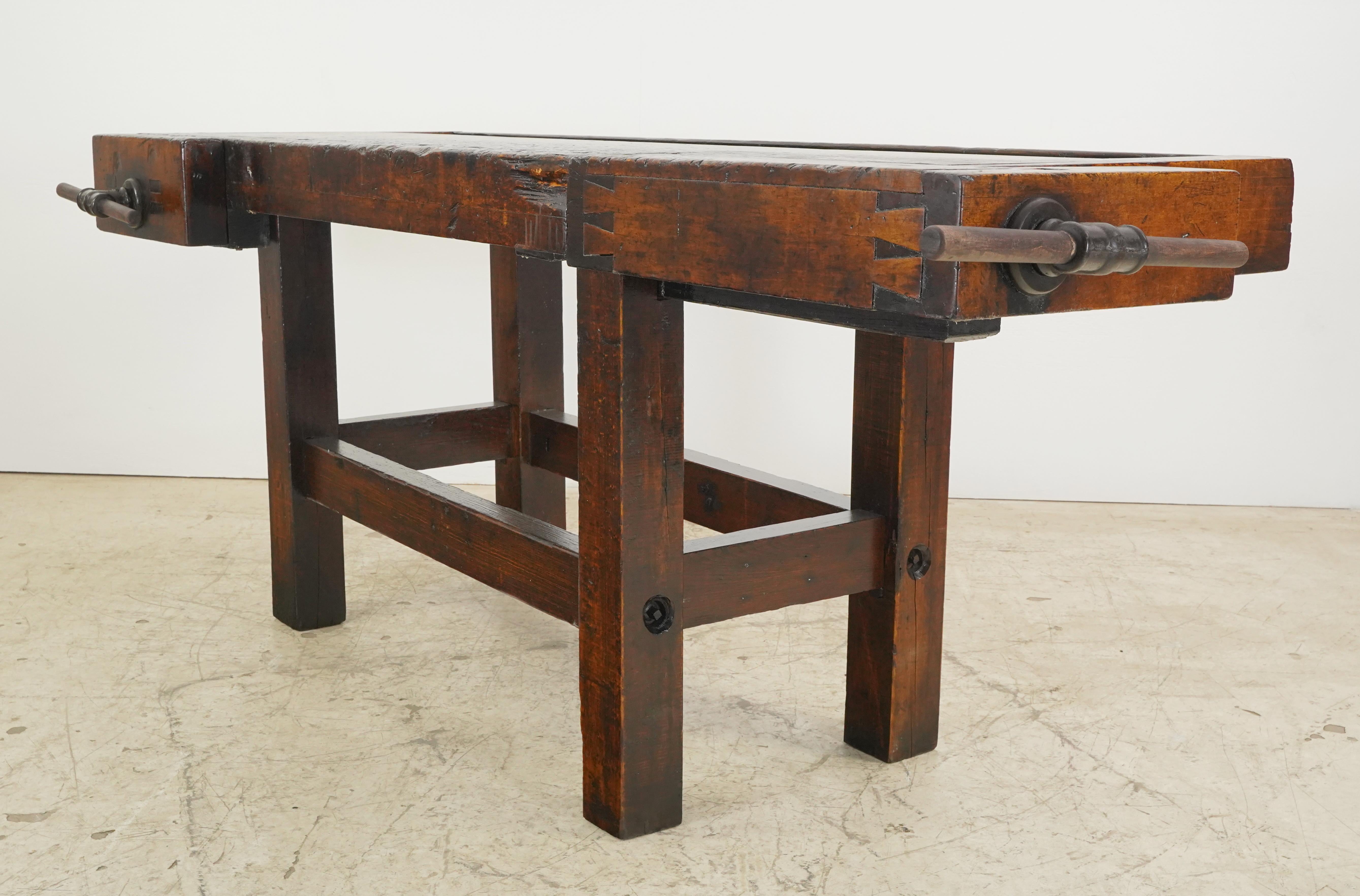 Construido con un grueso tablero de madera y patas unidas por una viga de soporte inferior. En el borde trasero hay un hueco para restos de madera y en el frontal varios agujeros para fijar las piezas. El banco de trabajo tiene dos tornillos de