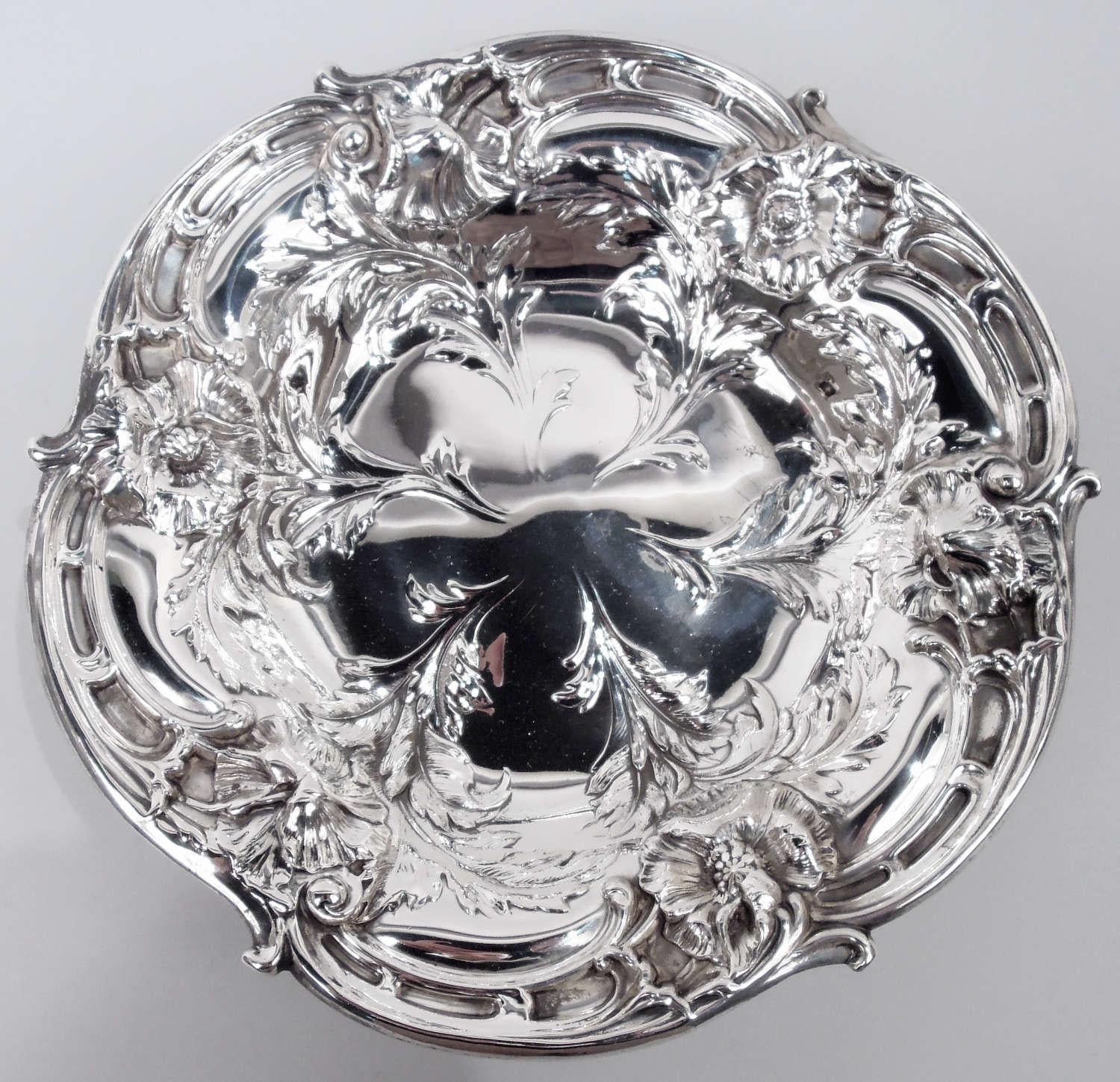 Art Nouveau sterling silver bowl. Made by Reed & Barton in Taunton, Mass. in 1949. Lobed well and scrolled rim. Chased ornament in form of flowers with stems terminating in well center (vacant). Four leaf-mounted scroll supports. Fully marked
