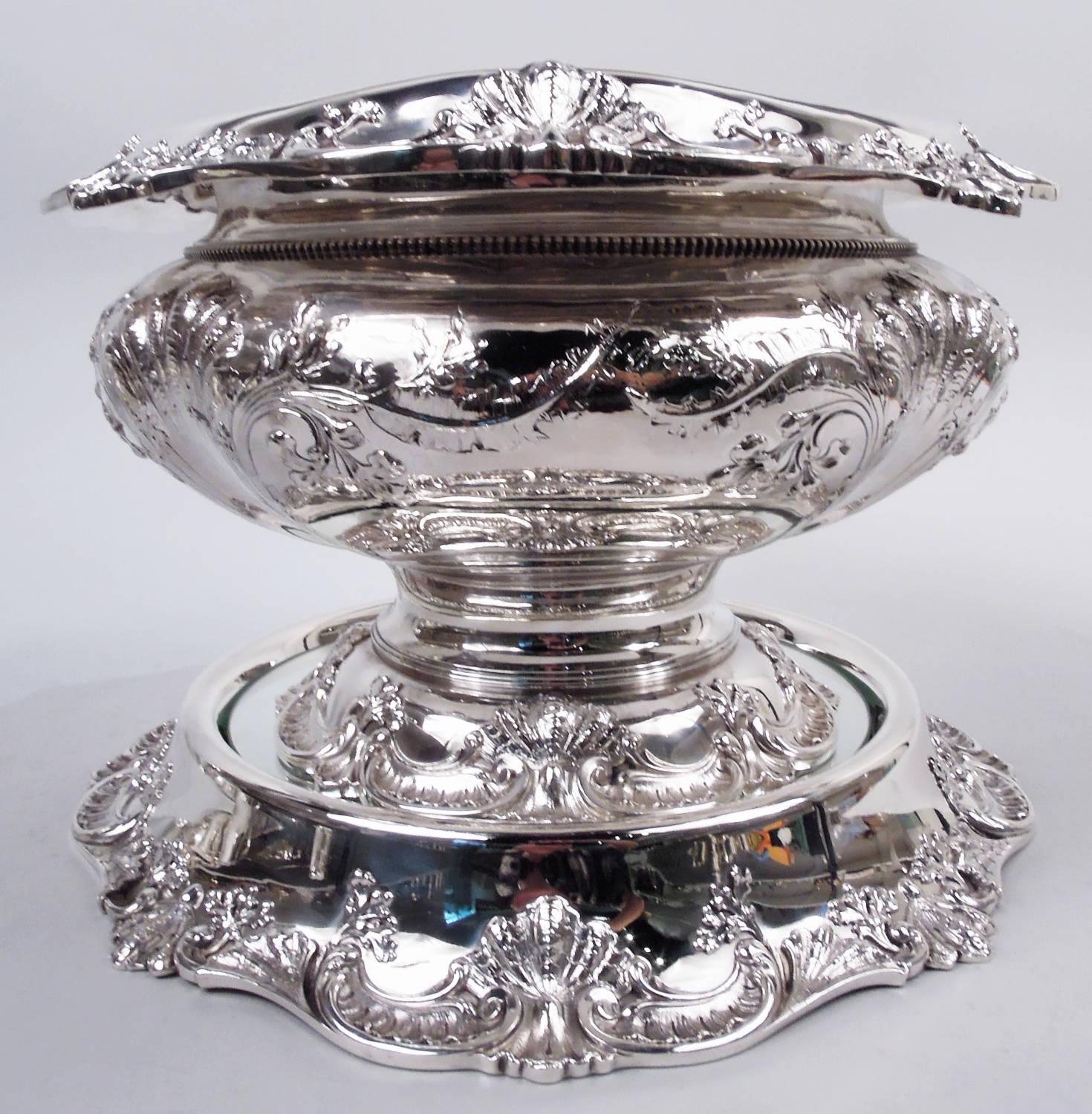 Ponchera clásica victoriana de plata de ley sobre meseta. Fabricada por Reed & Barton en Taunton, Massachusetts, hacia 1910. Cuenco panzudo y acanalado con borde de boca vuelto y volutas y pie elevado y volutas. La meseta tiene un pozo con espejos y