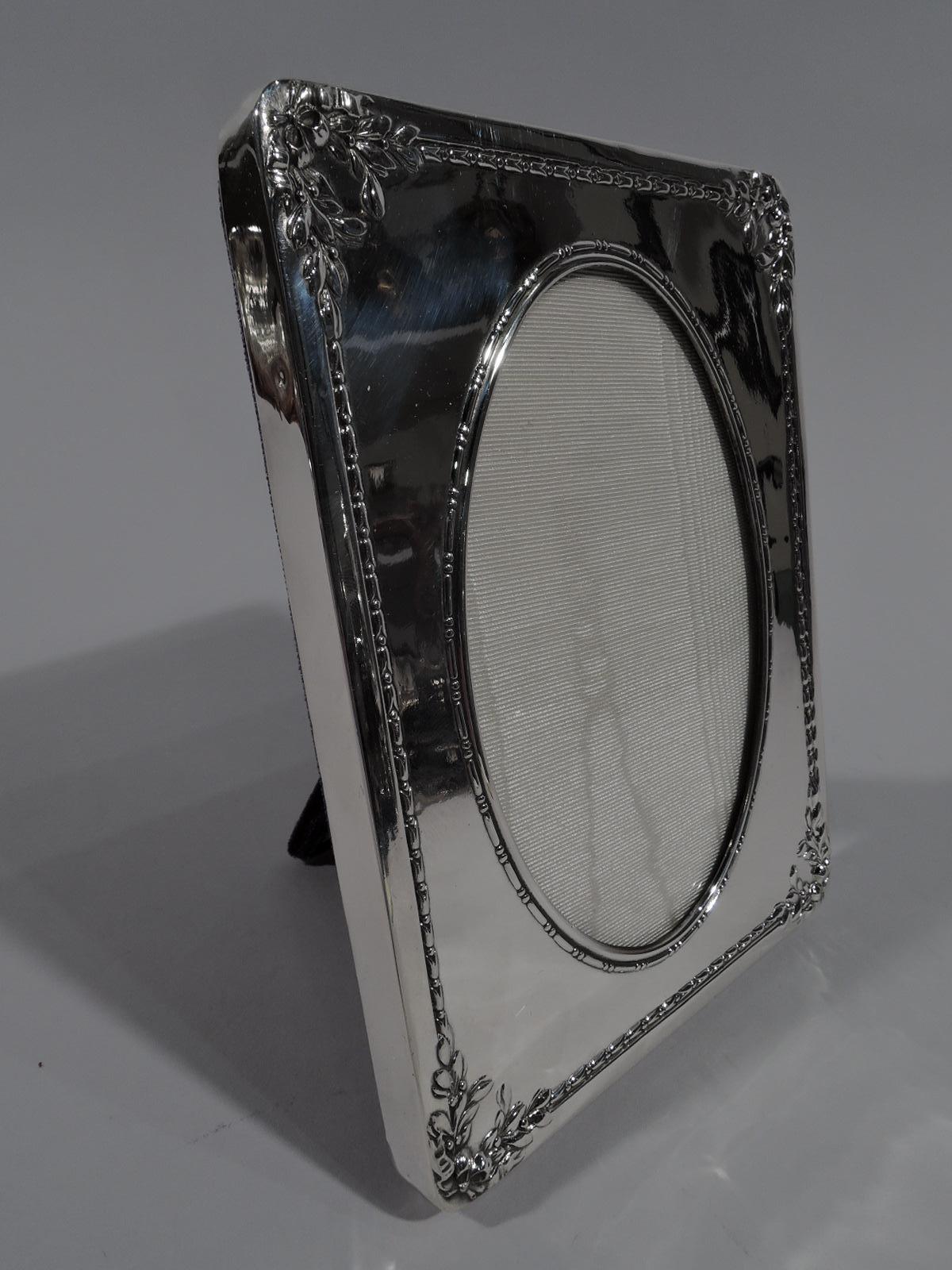 Edwardian sterling silver picture frame. Made by Reed & Barton in Taunton, Mass., circa 1915. Oval window with bead-and-reel border in rectangular surround with imbricated floral border; applied flat rim and ribbon-tied wreaths at corners. With