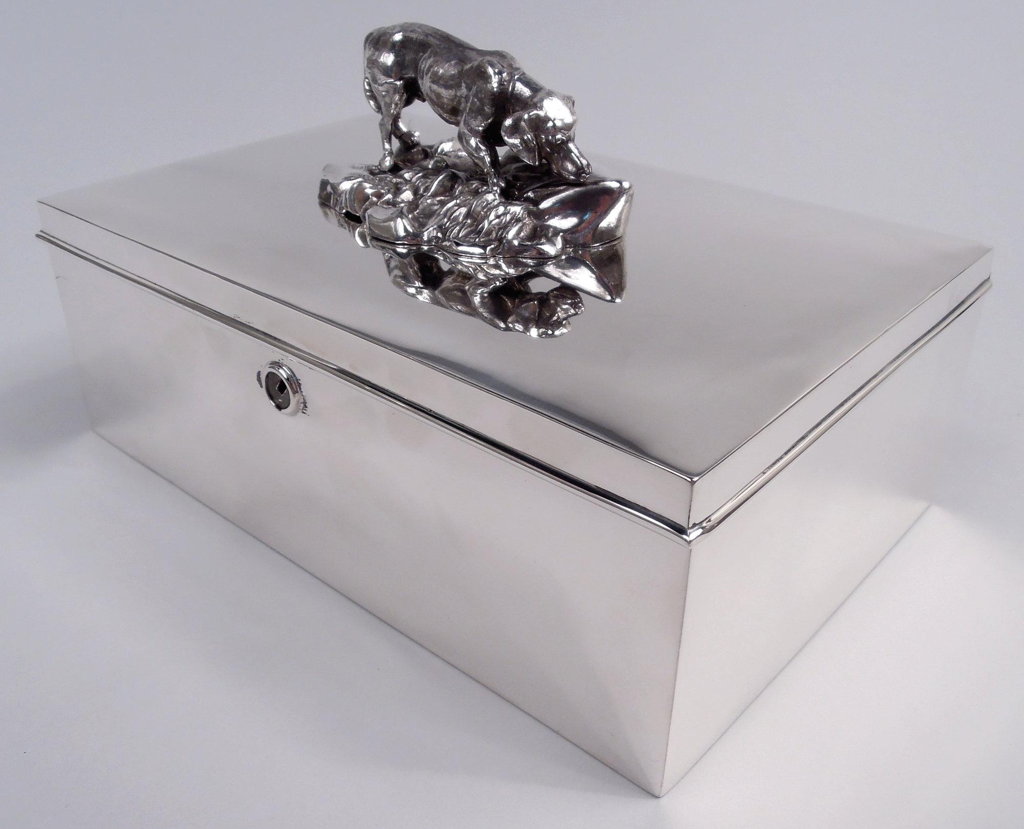 Modern sterling silver cigar box. Made by Reed & Barton in Taunton, Massachusetts, ca 1920. Rectangular with straight sides. Cover hinged with molded rim; on top, cast figural finial of hound snuffling around, nose to the ground. Interior gilt with