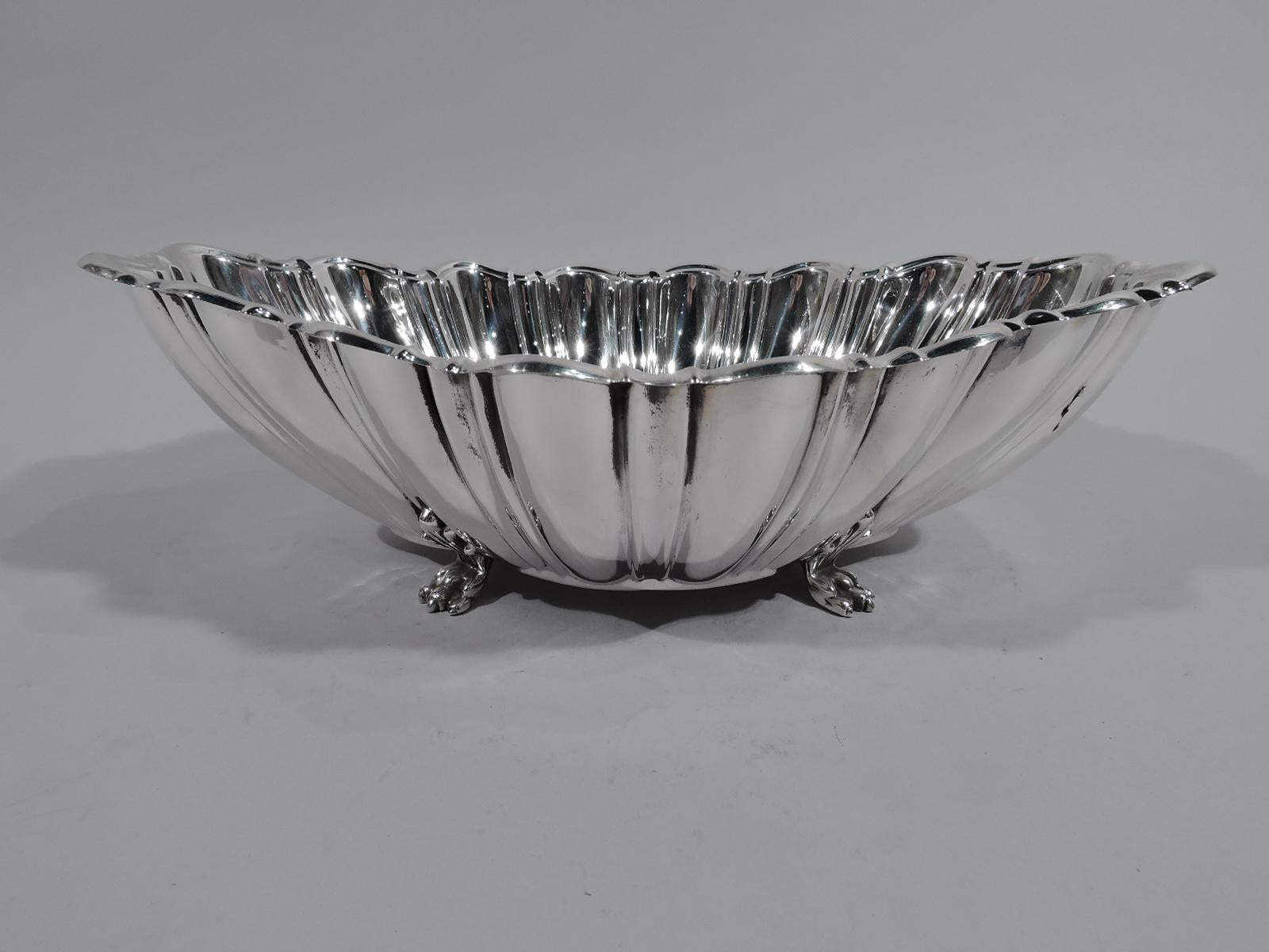 Modern classical sterling silver centerpiece bowl. Made by Reed & Barton in Taunton, Mass. in 1950. Quatrefoil well. Curved sides with alternating flutes and lobes. Scrolled rim. Rests on 4 scallop-shell mounted paw supports. A great revving up of
