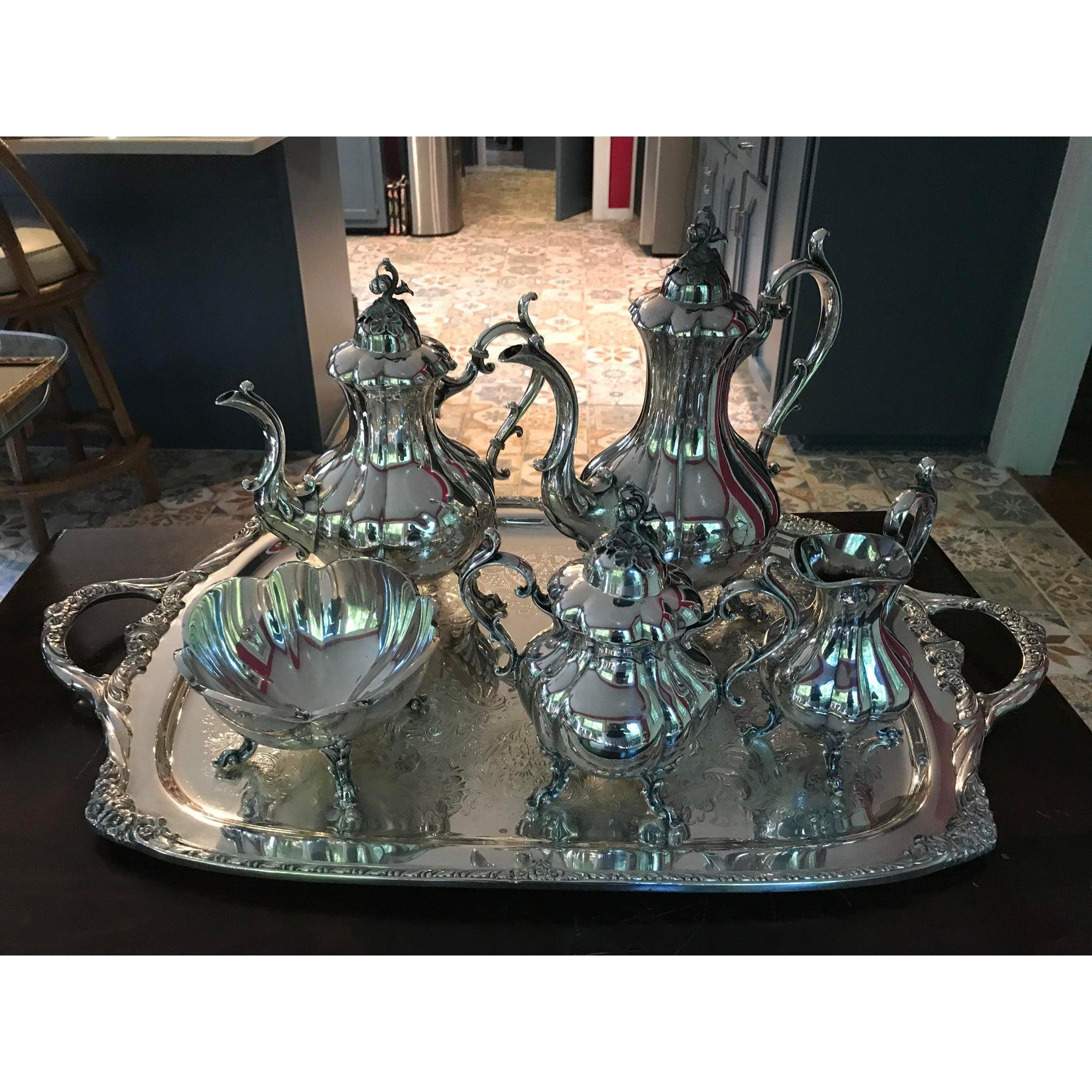 The image shows a vintage Reed & Barton 1795 Winthrop 5-piece tea set in silver plate. This set typically includes: 
A teapot
A coffee pot
A sugar bowl with a lid
A creamer
A waste bowl
The Winthrop pattern, dating back to around 1950, is known for