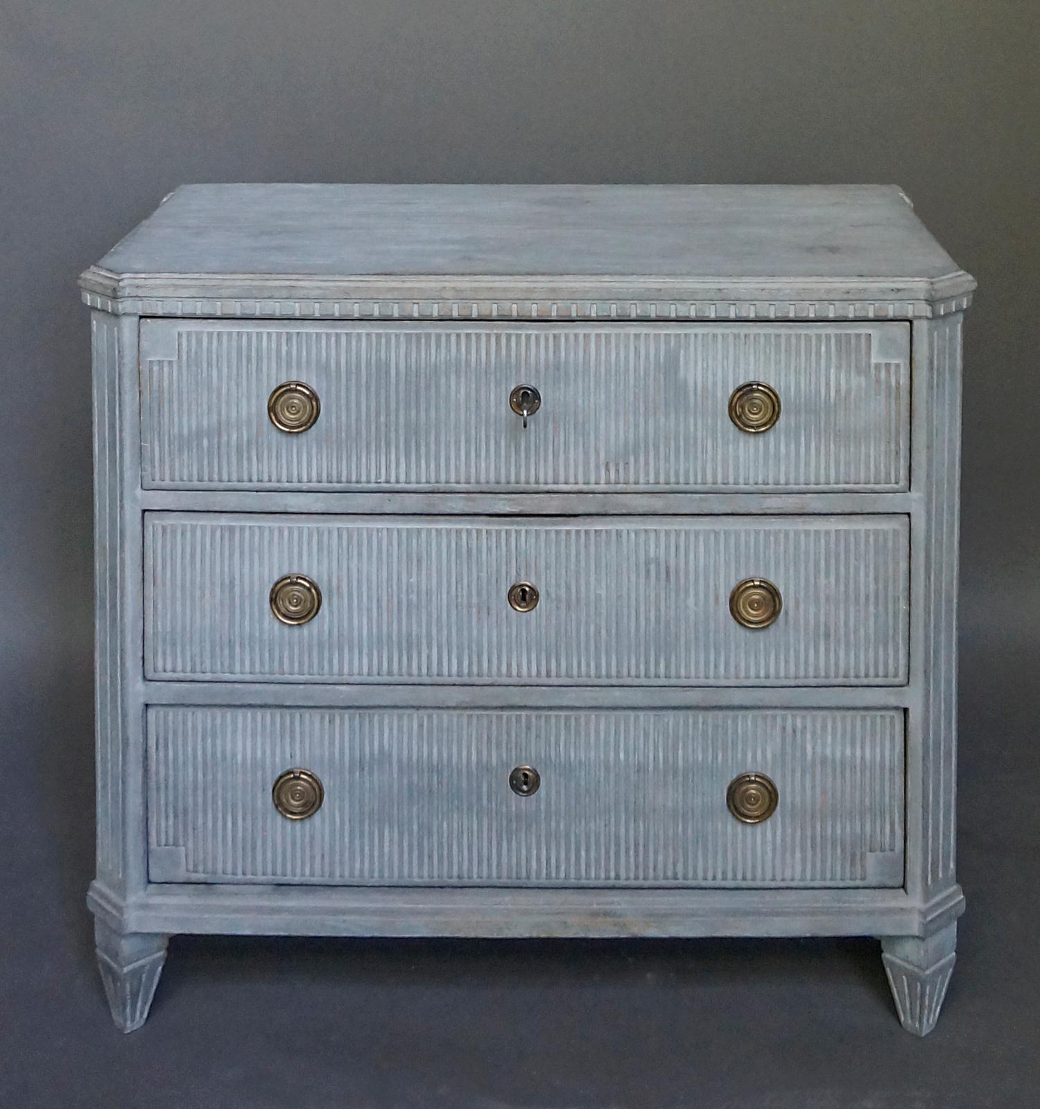 Swedish three-drawer chest in the neoclassical style, circa 1890. The drawer fronts have an overall reeded pattern with notched corners. Shaped top with dentil molding, canted corners, and tapering square feet. Brass pulls and escutcheons. Later