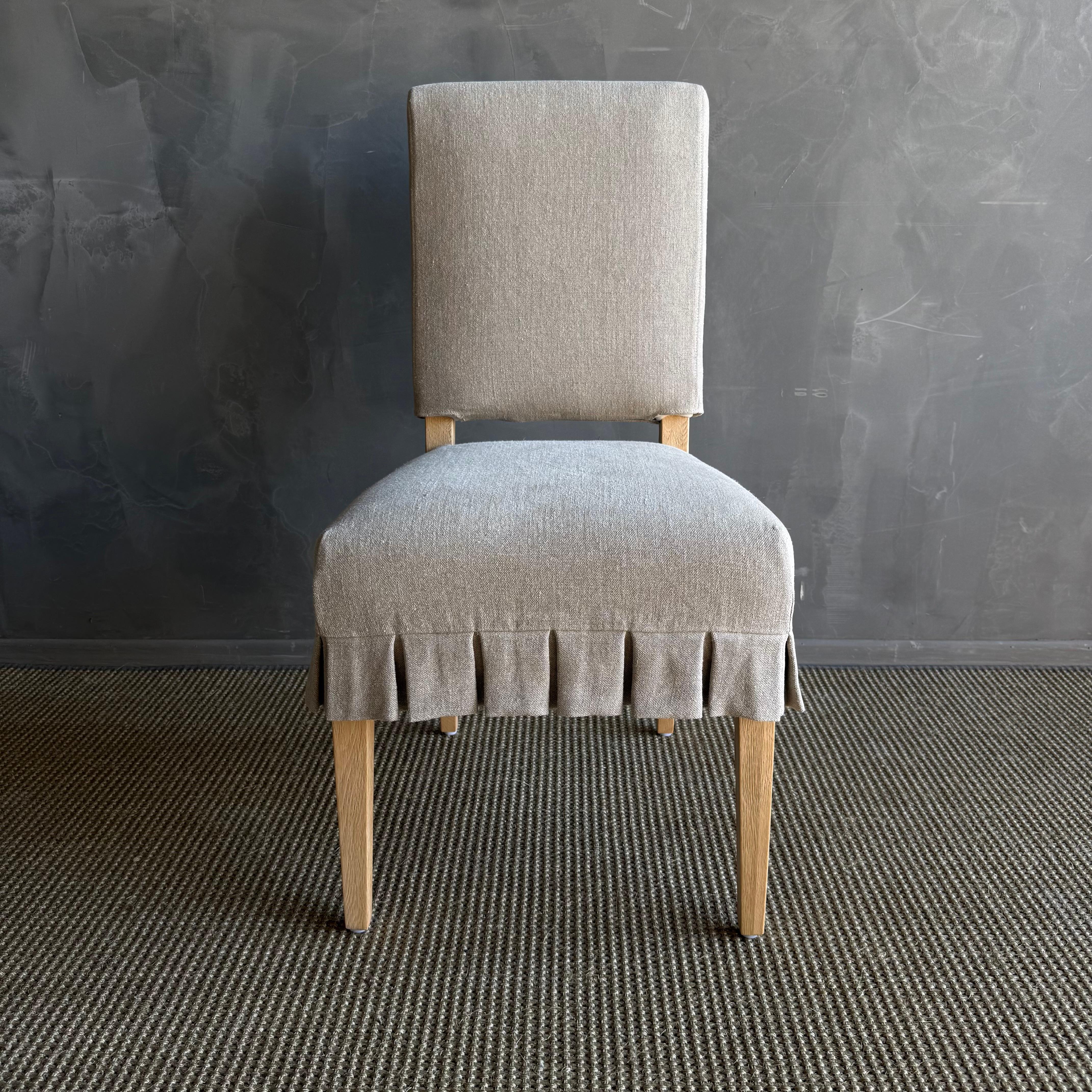 Introducing the elegant Reese white oak dining chairs, featuring custom slipcovers crafted from luxurious Belgian linen. These chairs showcase a timeless design enhanced by pleated ruffle skirts, adding a touch of sophistication and charm to your