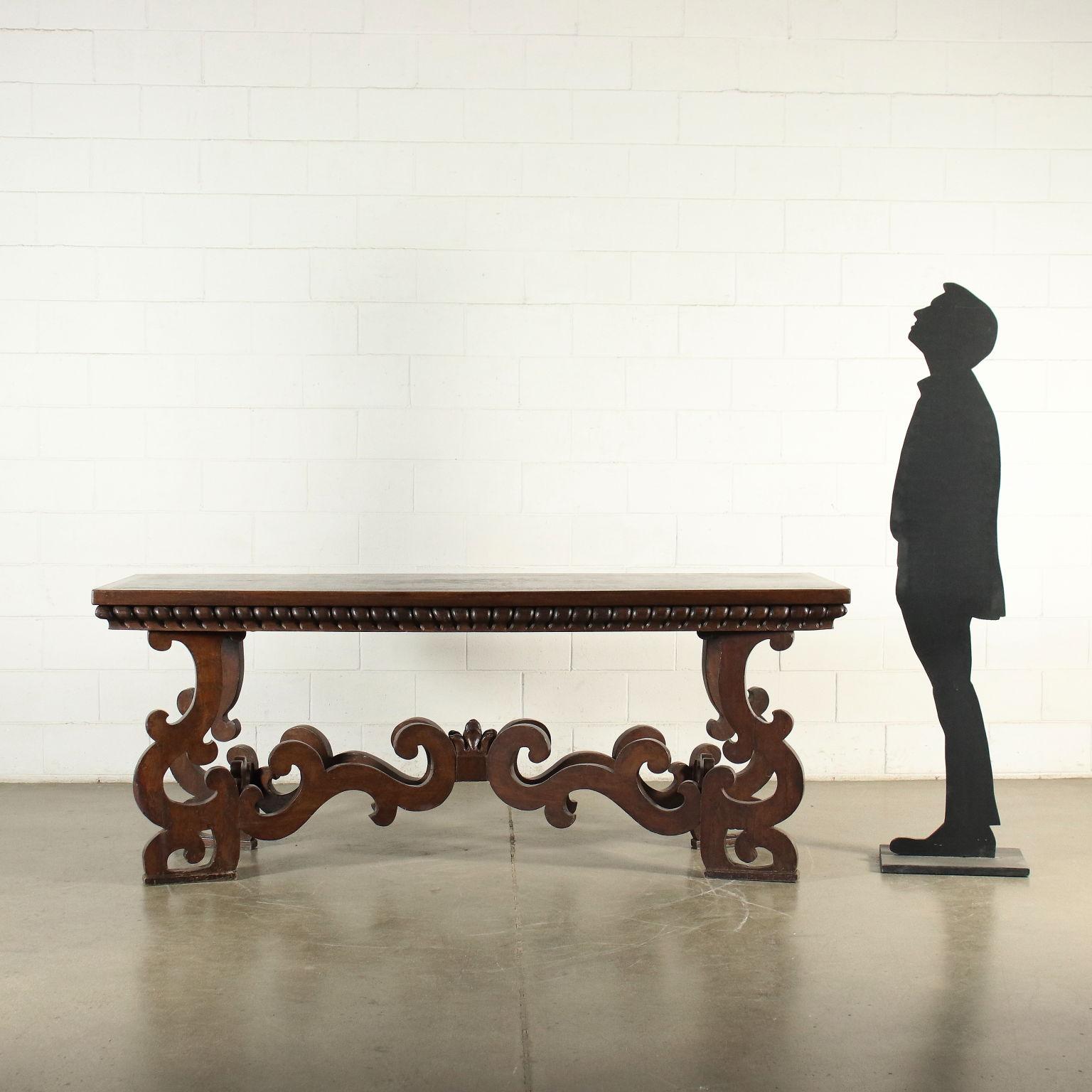 Baroque refectory table, supported by legs carved in volutes, connected by cross stretchers, also in volutes and with a central leafy element; under the top there is a carved frame with a pod pattern. In walnut, the single-axis top was subsequently