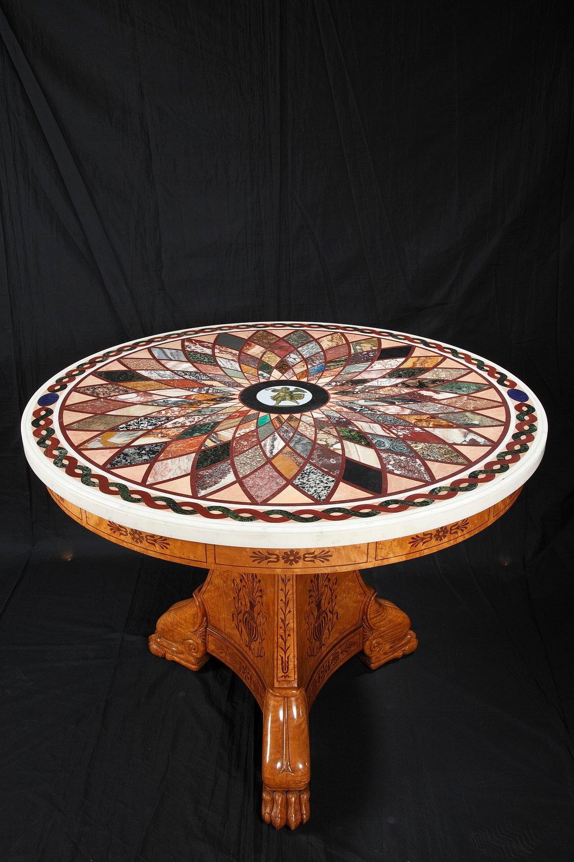 A Charles X period veneered wood center table resting on a central foot ended with three imposing claw-feet. The base and the belt of the table are adorned with wood marquetry decoration showing palms, vases and foliage garlands.

A remarkable