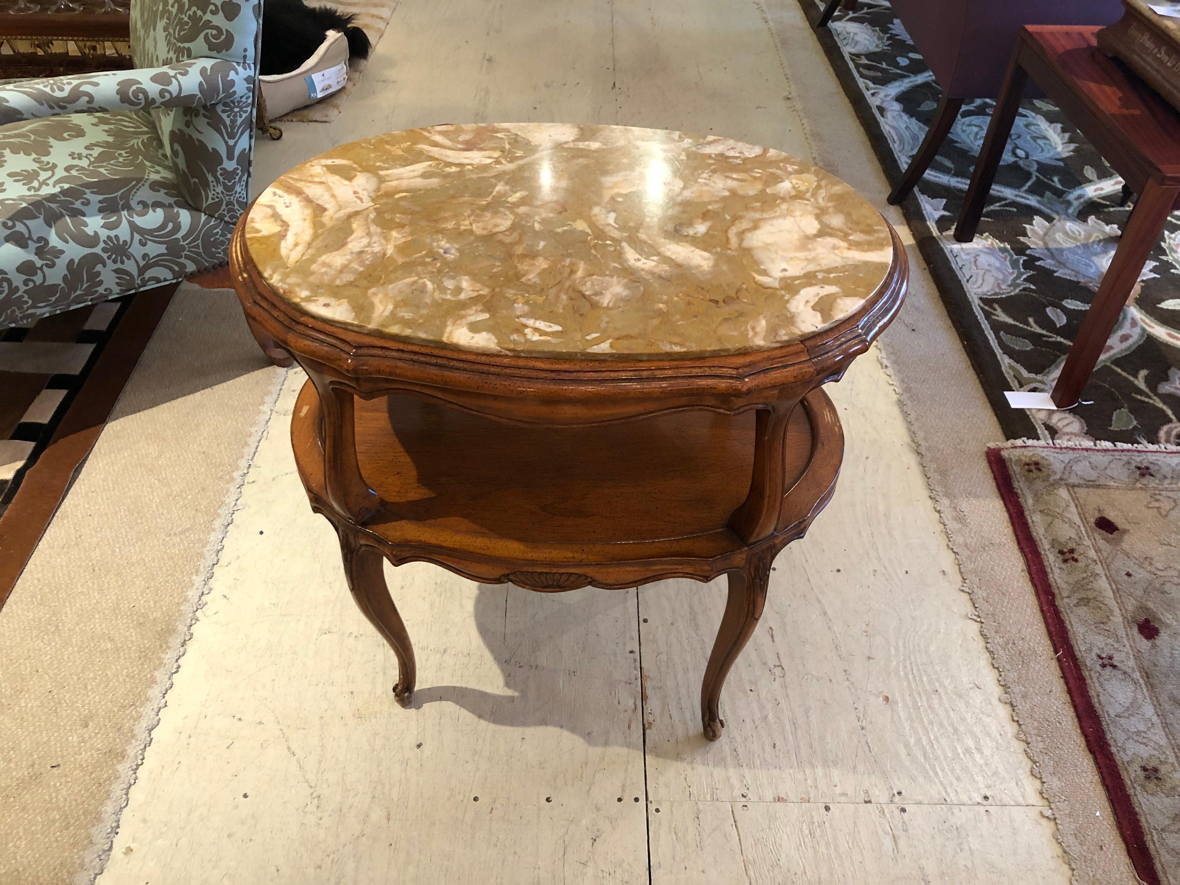 French Provincial style marble inset two-tiered oval side table having handsome carved wood with cabriole legs and scalloped apron beneath the bottom tier. Marble is a luscious caramel and cream. Makes a great stationary bar. 2nd tier 17 H from