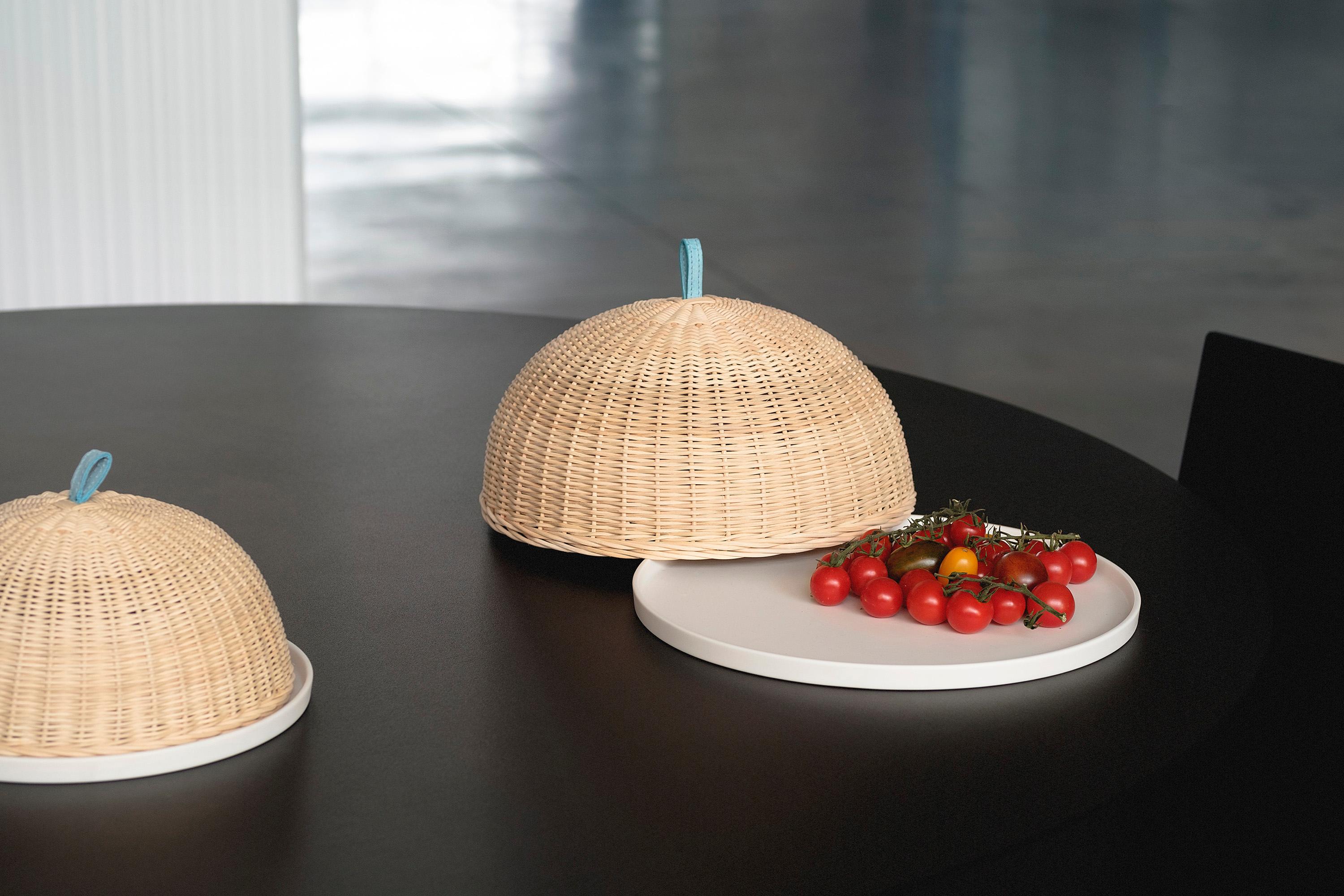 Like a pergola shelters from the sun on hot summer days, in this piece the wicker dome protects the contents of the porcelain tray.
The tray is minimal and characterized by a matte finish wich makes it pleasant to the touch, the covering is