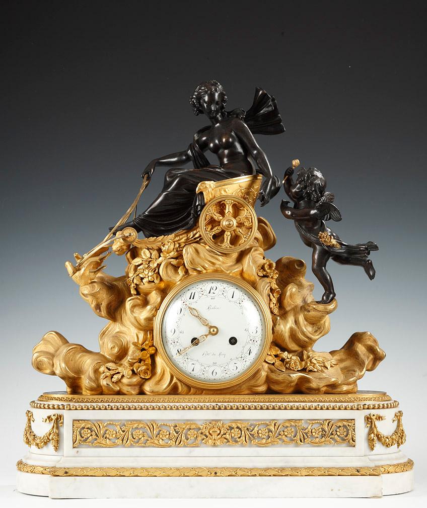 Inscribed on the dial Robin, Hger du Roy.

A Louis XVI style clock set, made in patinated bronze and gilded bronze, made up of a mantel clock ornated with the figures of Venus and Cupid, seated on her doves-drawn chair; the clouds forming the case