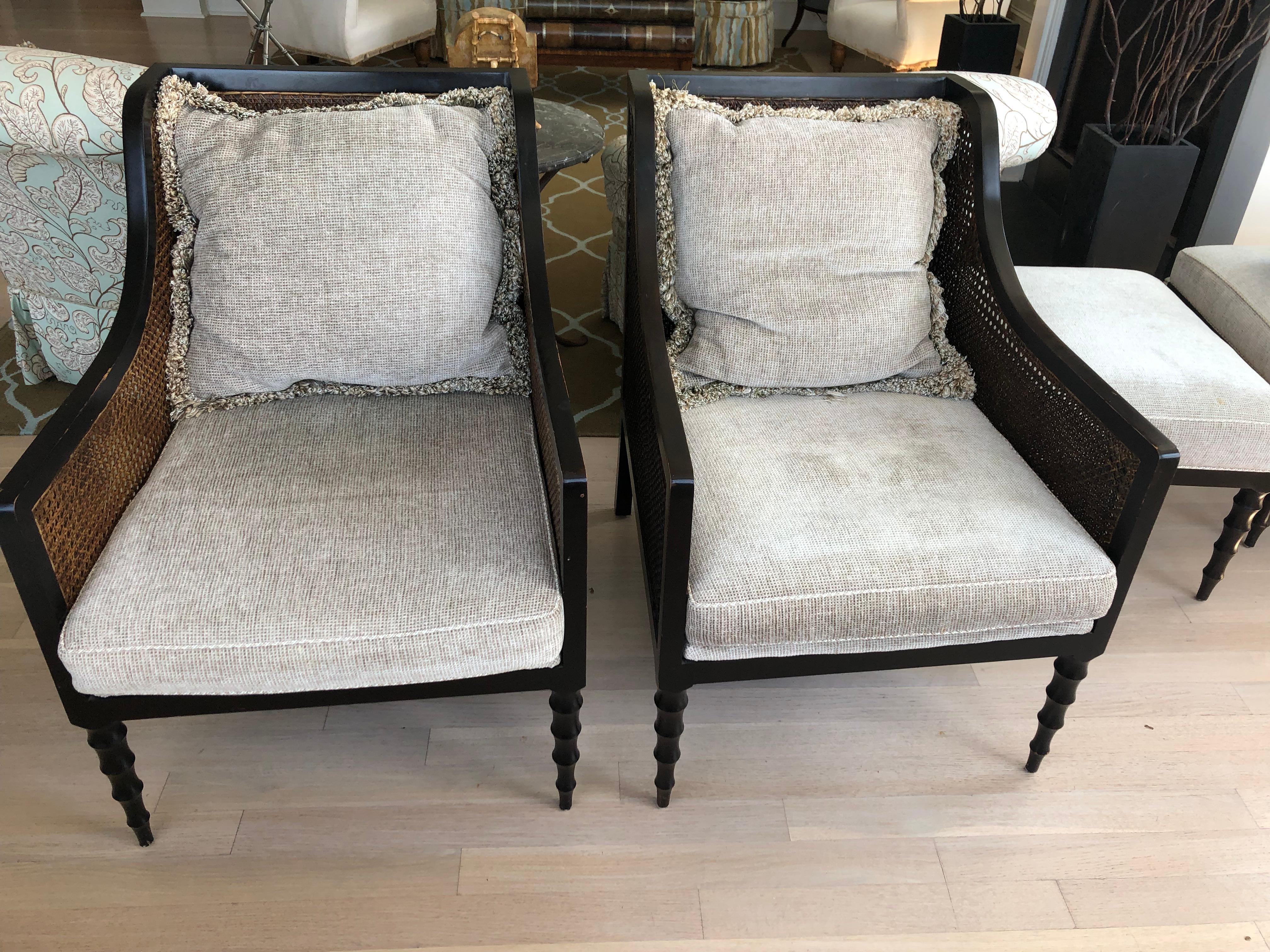 Stylish and refined Indonesian pair of ebonized and natural colored double caned club chairs having beige chenille removeable seat and back cushions and turned carved legs. There are a set of matching rectangular ottomans included, 25.5 W 19 D 17.5