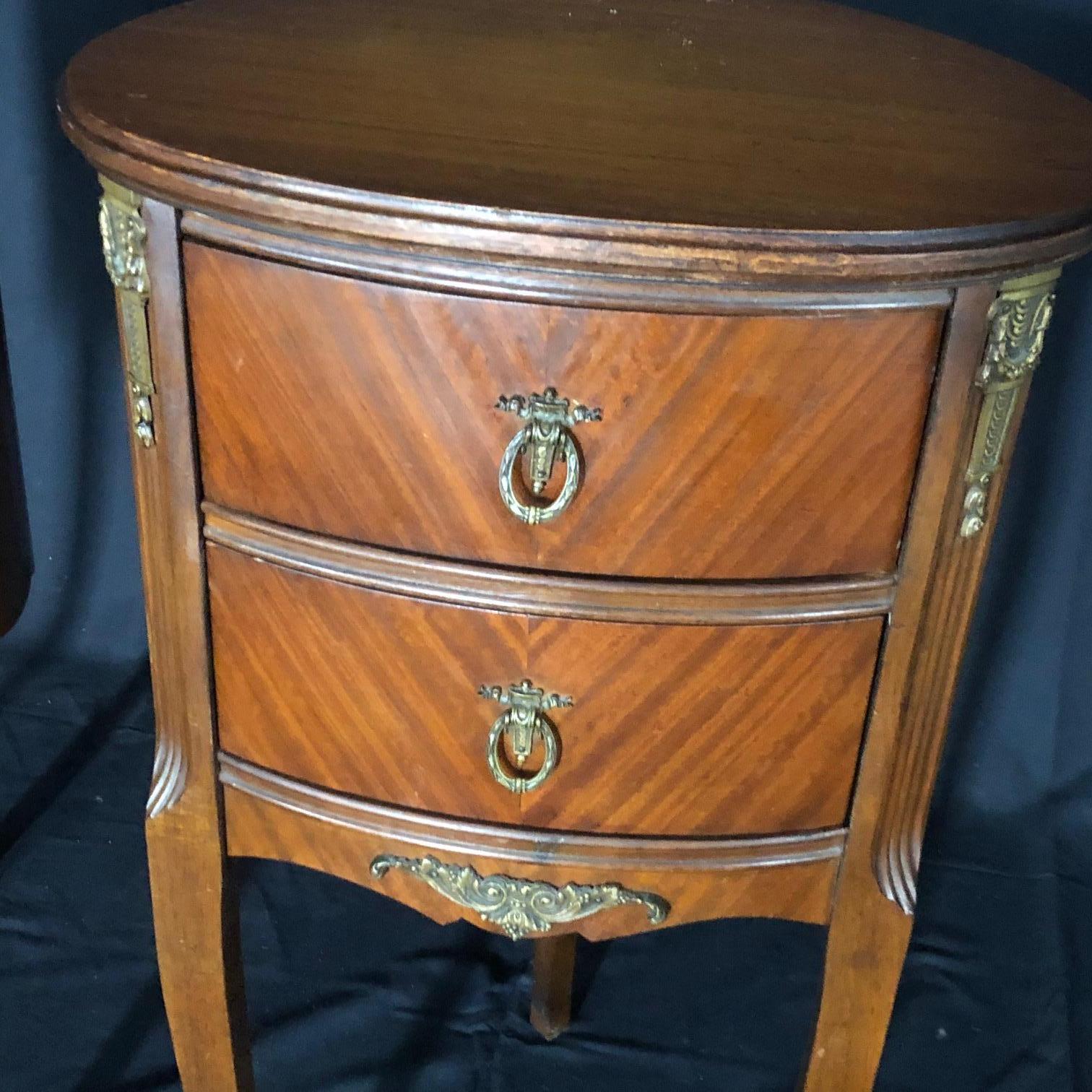 Pair of mahogany Louis XV oval style nightstands having three legs, original brass pulls and side mounts as well as scroll feet. The two drawers on each stand are beautifully adorned with wreath and ribbon pulls over aprons with grape leaf and